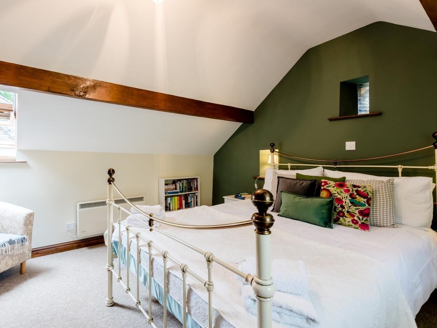 A bedroom with a white metal bed frame, a green wall, a bookshelf, and a window.