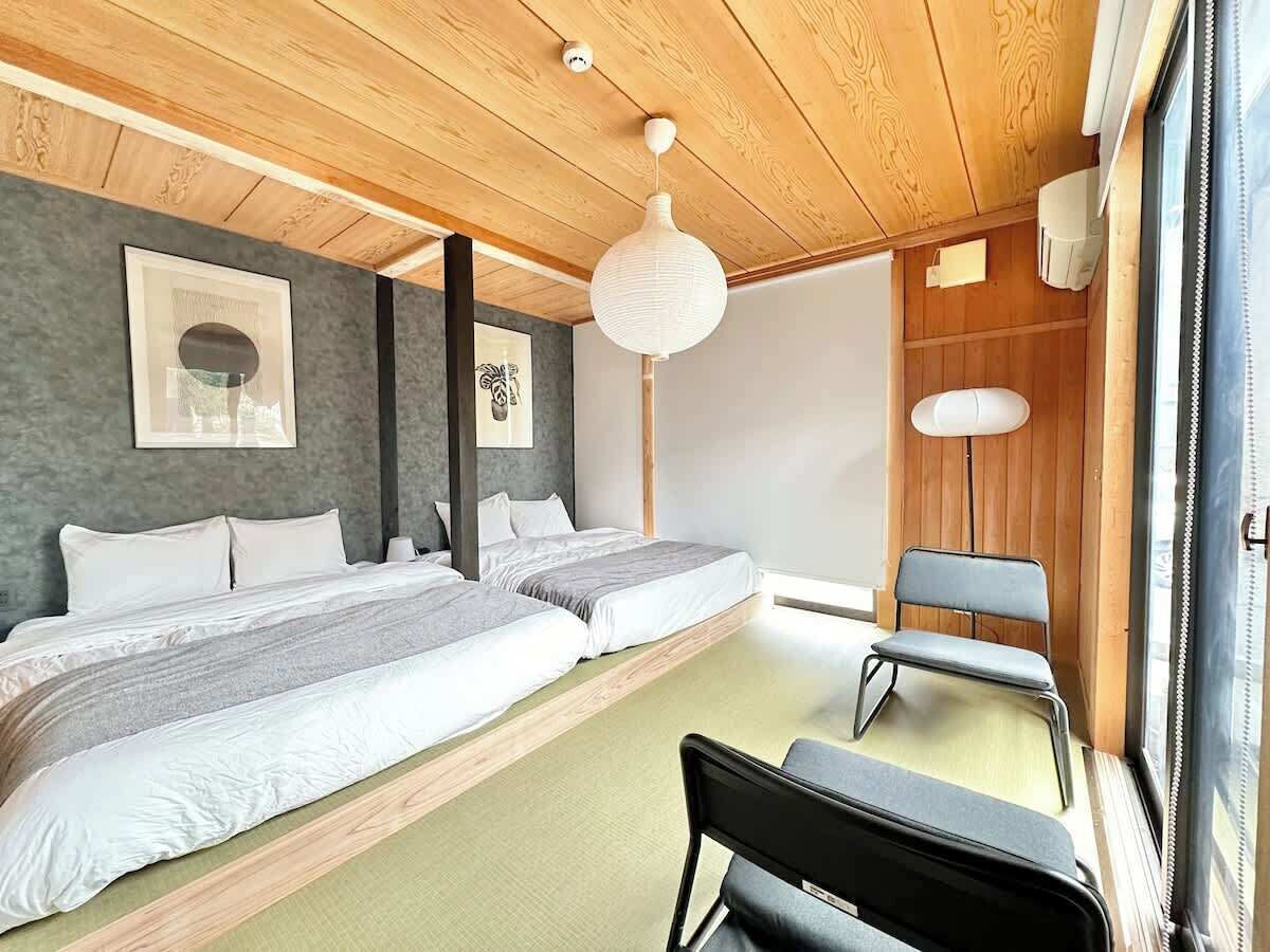 A modern bedroom with two beds, a sitting area, and a large window.