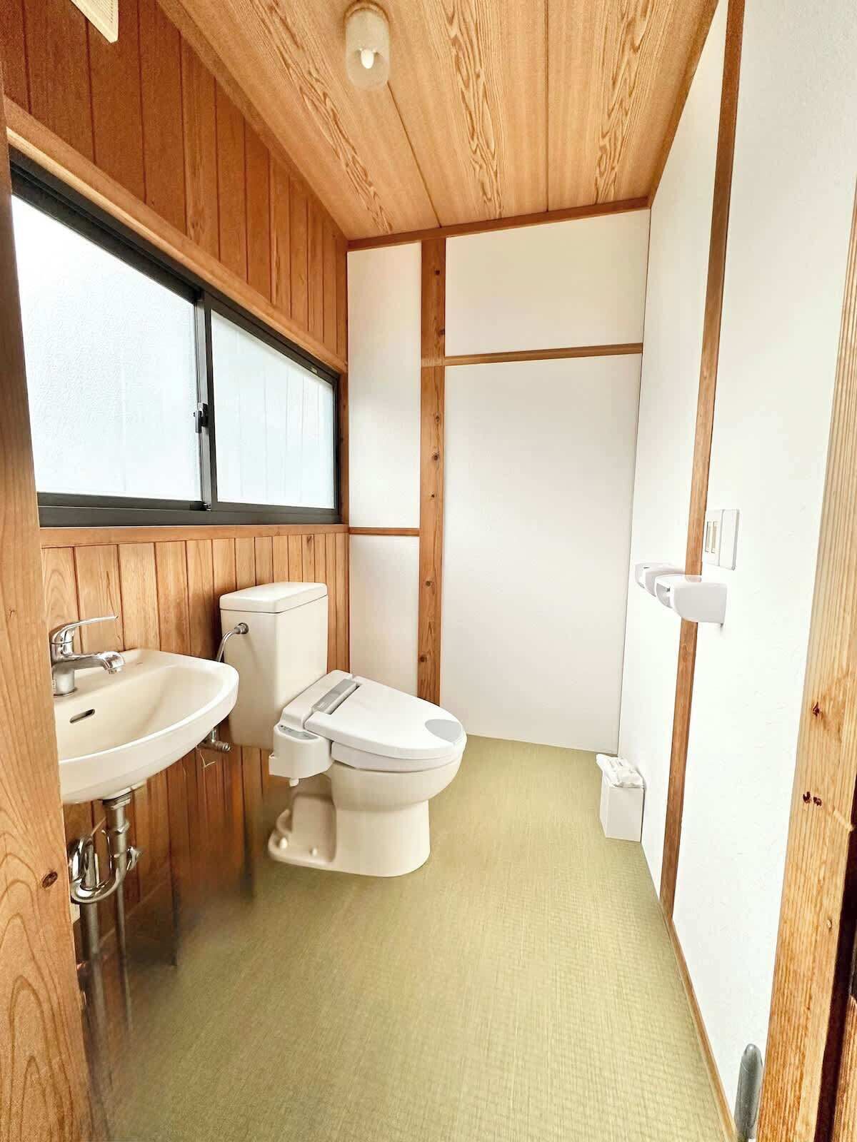 A compact, modern bathroom with wooden paneling, a toilet, sink, and a window.