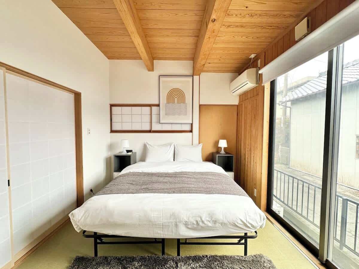 Un dormitorio con techo de madera, una cama grande, mesitas de noche, un ventanal con vistas y una obra de arte enmarcada en la pared.