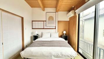 Un dormitorio con techo de madera, una cama grande, mesitas de noche, un ventanal con vistas y una obra de arte enmarcada en la pared.