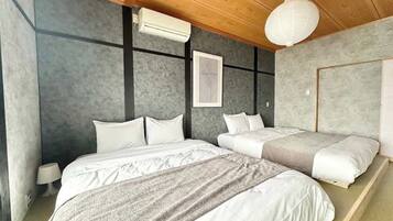 A bedroom with a large bed, a smaller bed, and a nightstand. There is a ceiling fan and a wall-mounted air conditioner.