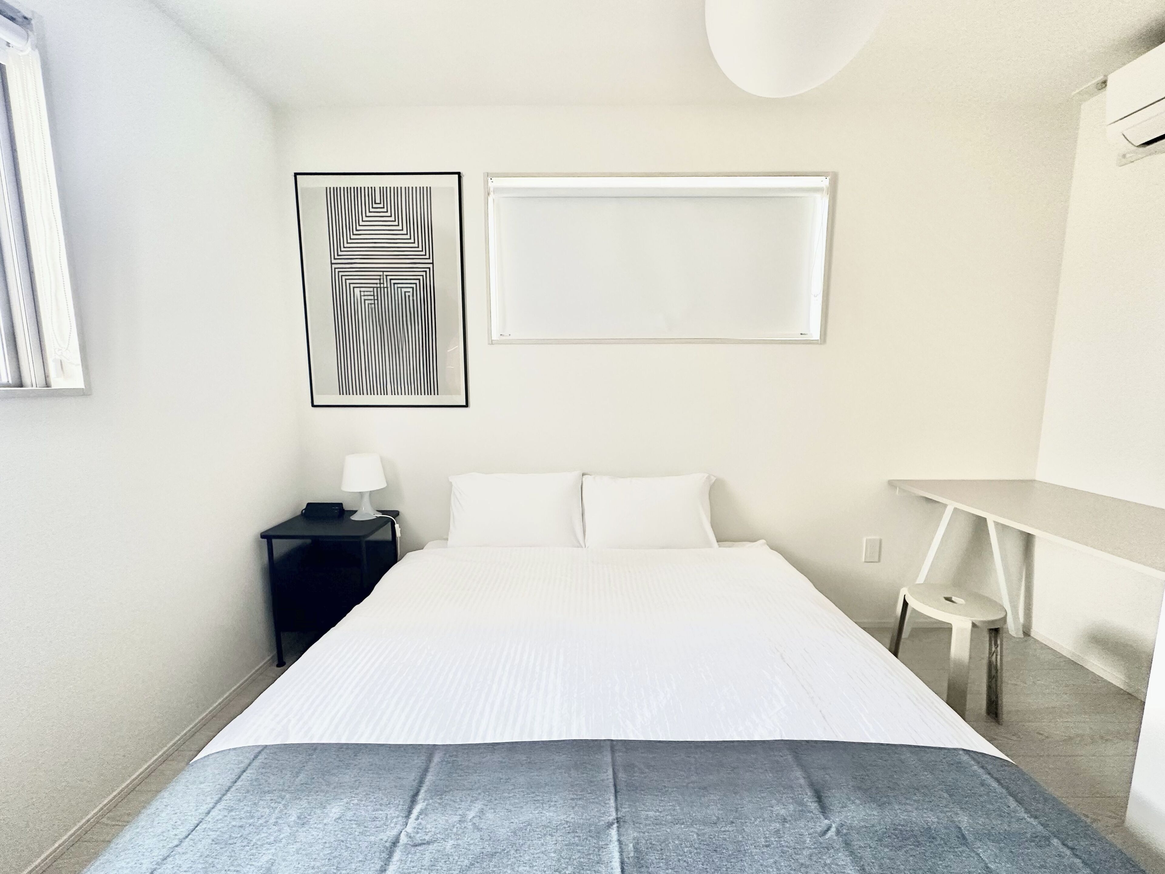 A hotel room with a bed, a nightstand, a lamp, a wall-mounted picture, and a small table.