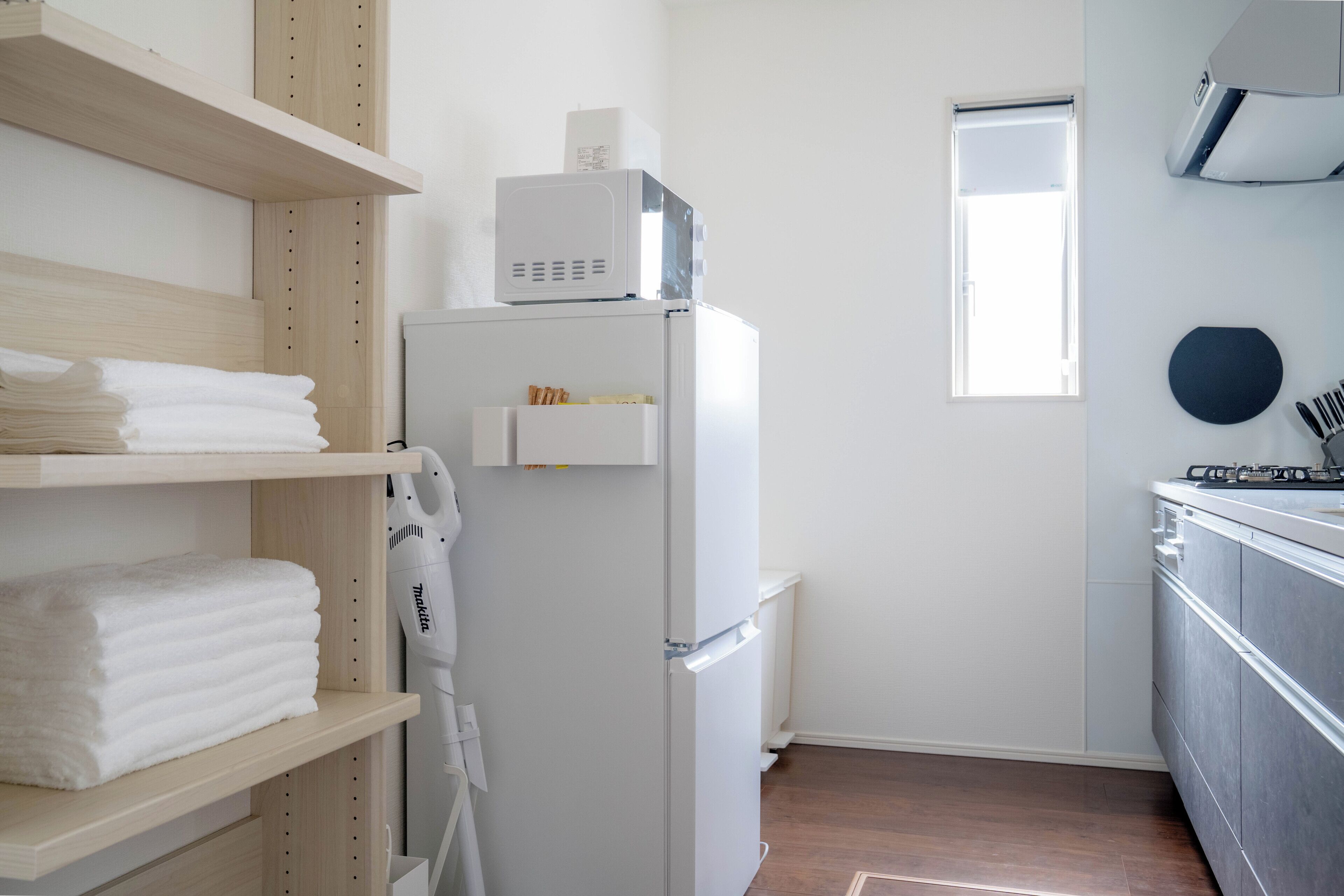 Una cocina compacta con un refrigerador blanco, estantes de madera con toallas, y una ventana.