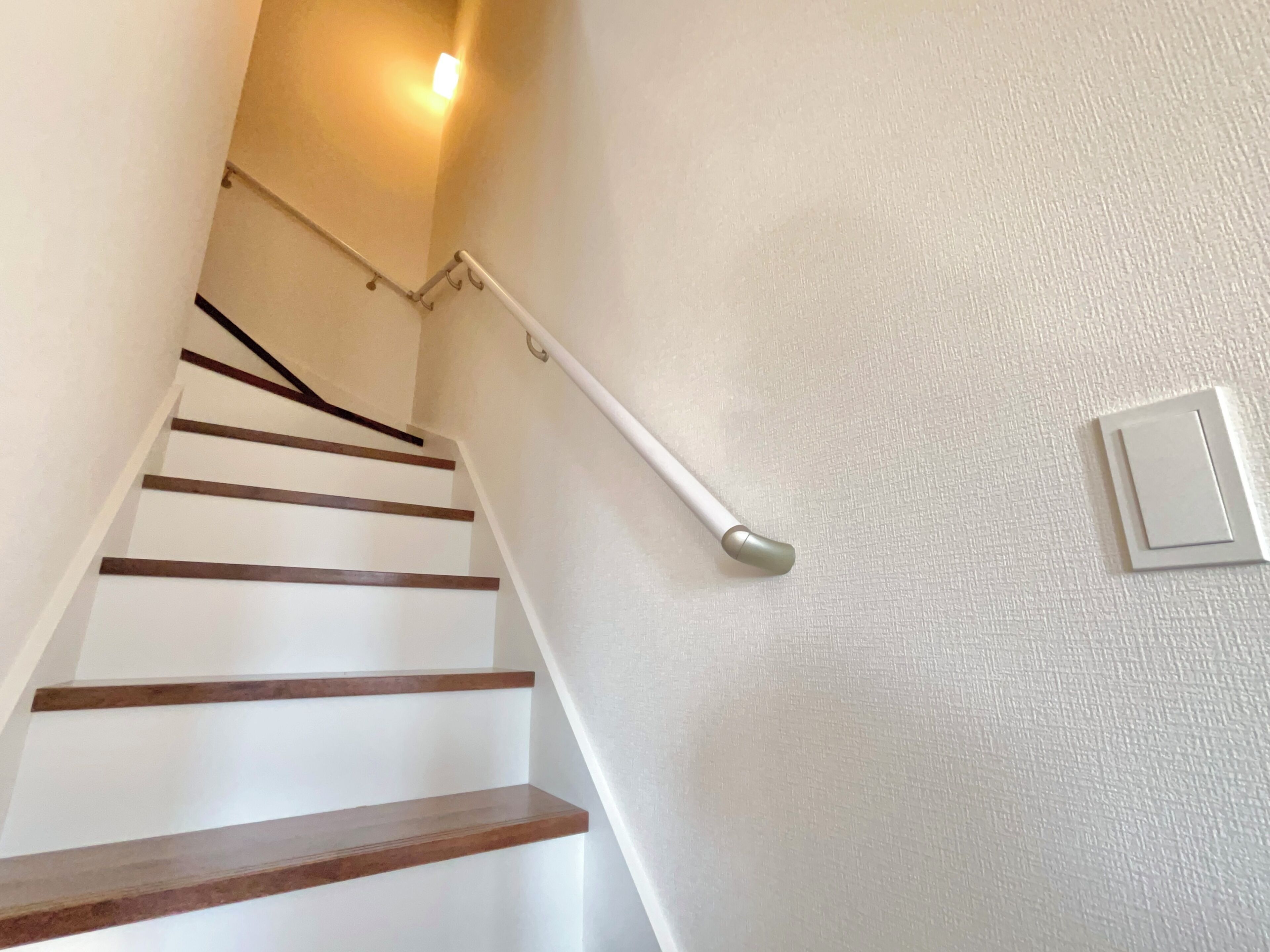 A staircase with wooden steps and a handrail, leading to a landing with a light switch on the wall.