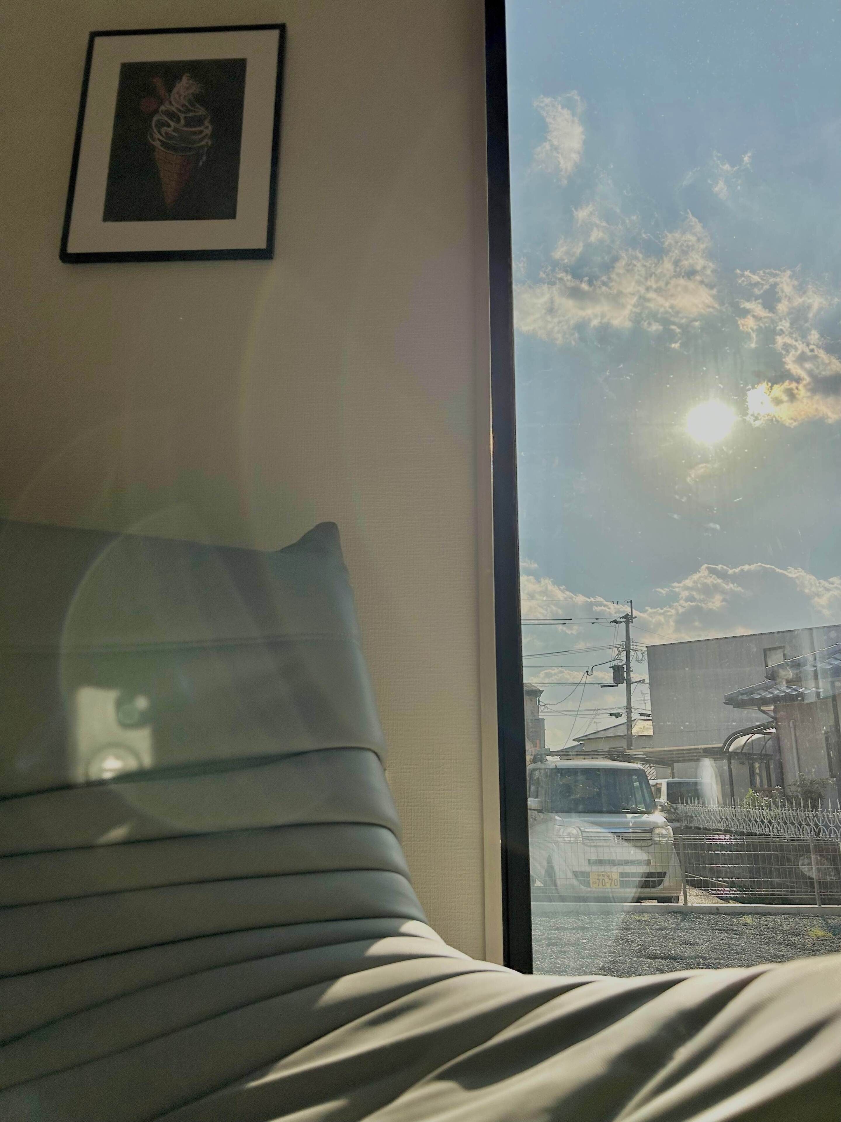 A room with a bed, a framed picture on the wall, and a window with a view of the street and buildings outside.