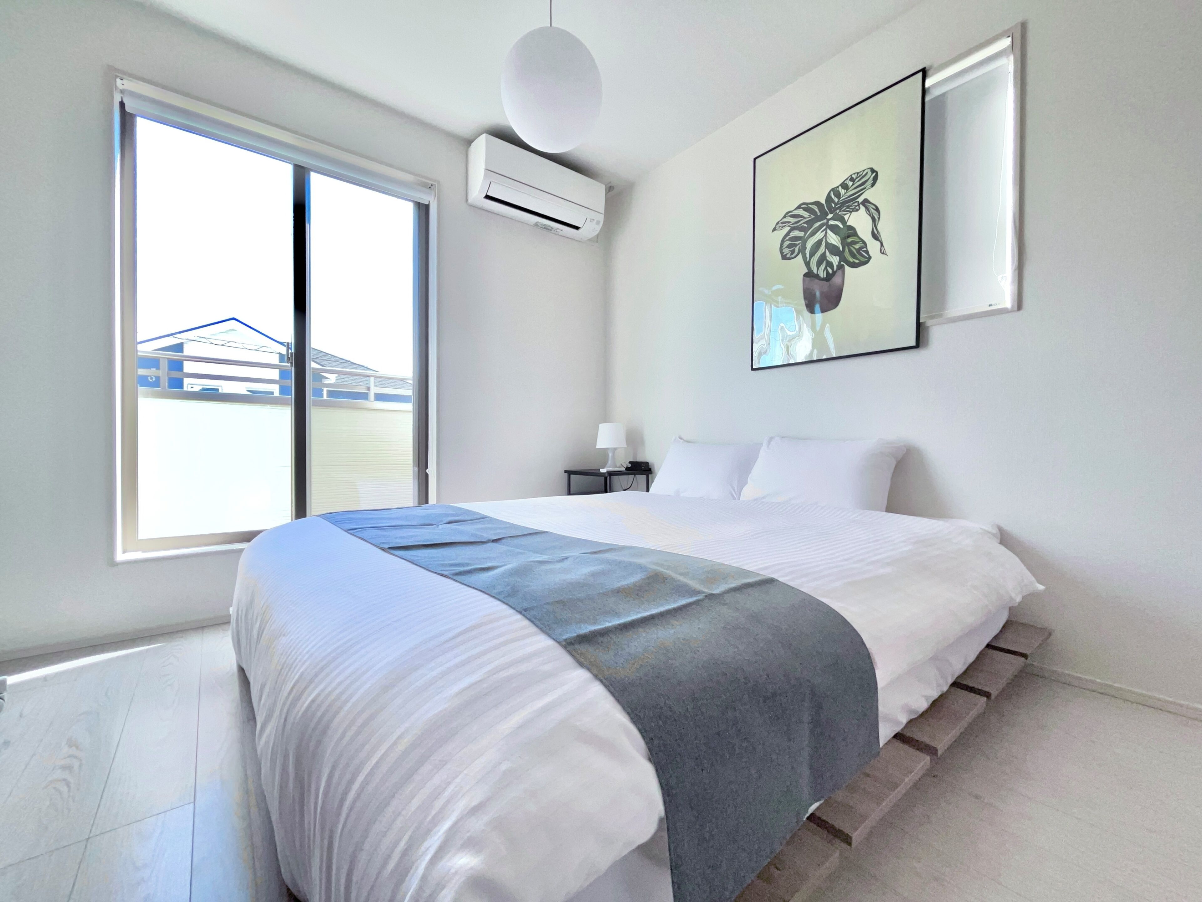 A bedroom with a bed, a window, an air conditioning unit, and a wall-mounted picture.