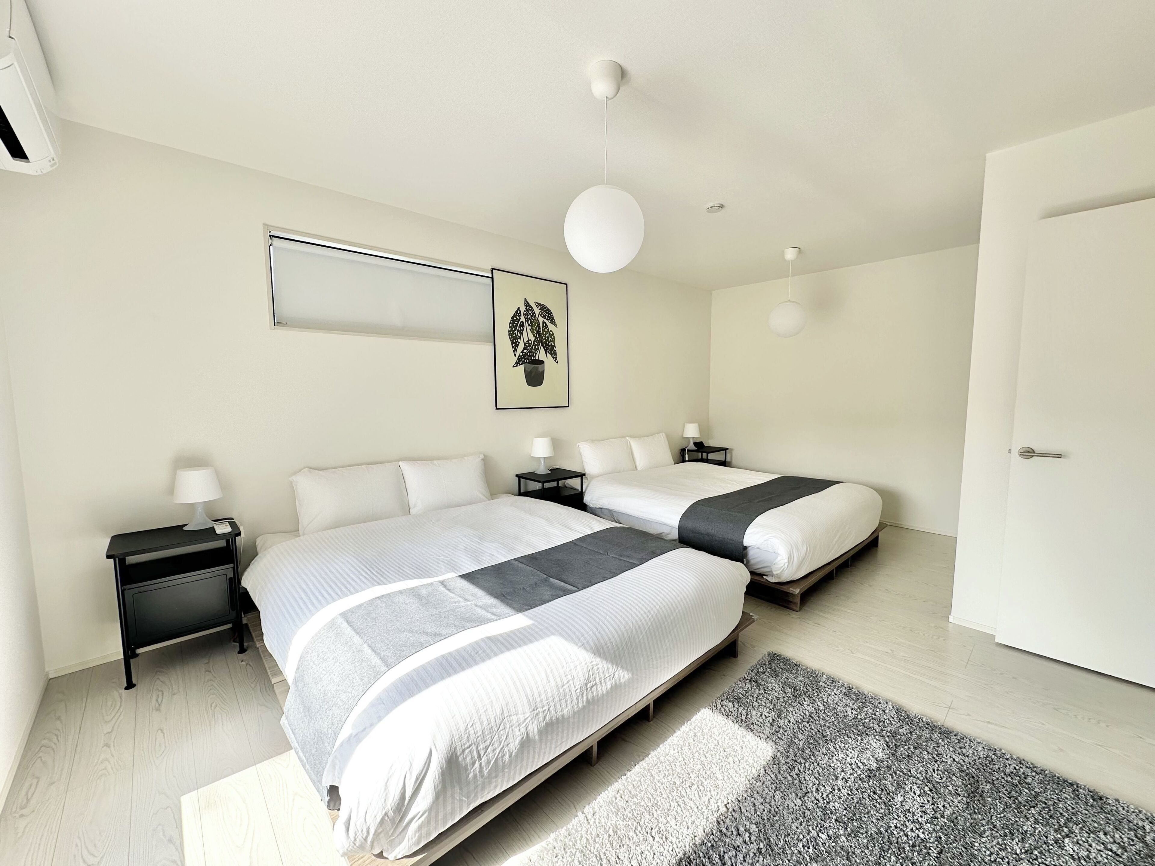 A modern bedroom with two beds, bedside tables, a hanging light, and a framed picture on the wall.