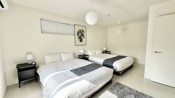 A modern bedroom with two beds, bedside tables, a hanging light, and a framed picture on the wall.