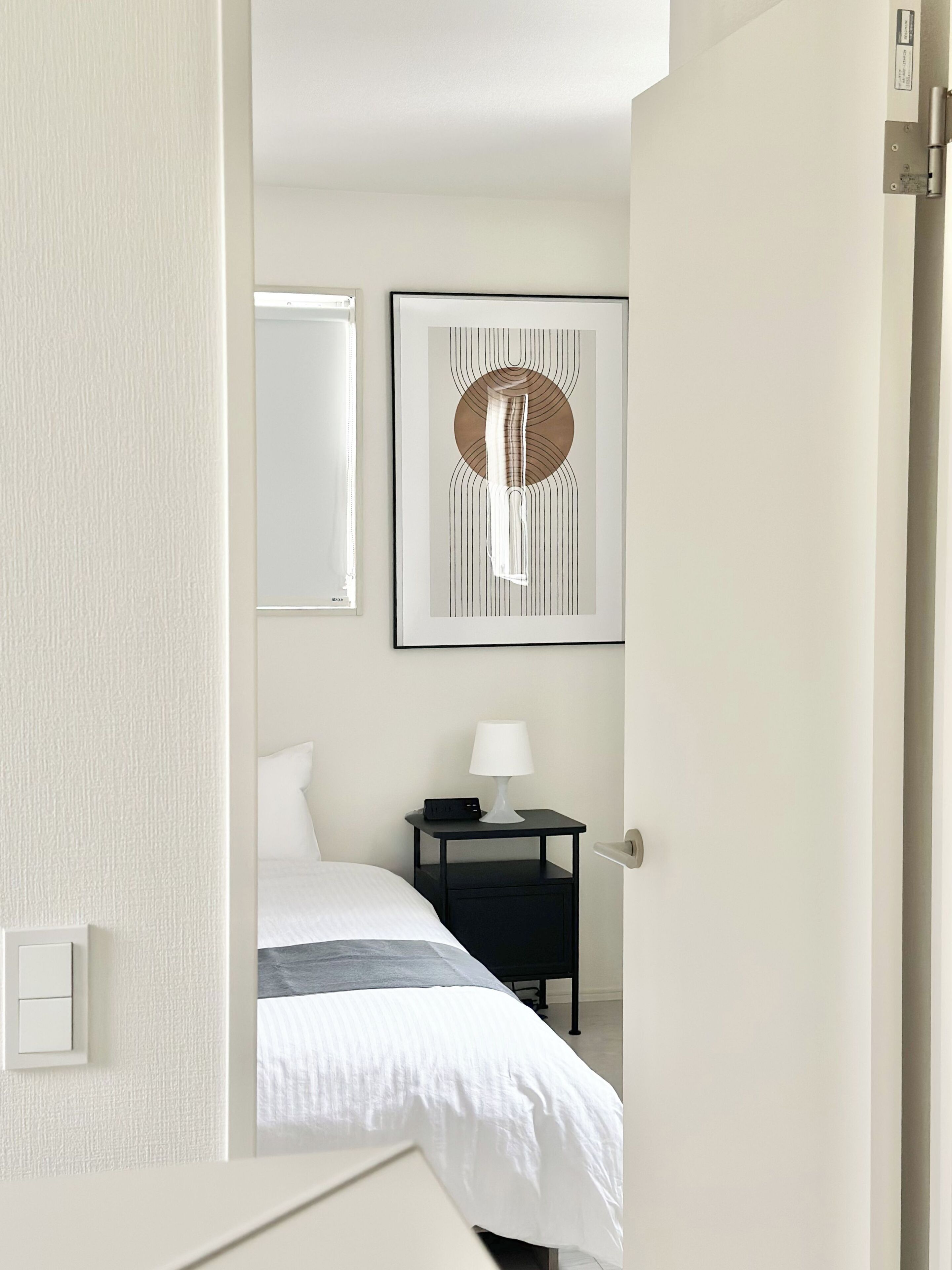 Ett hotellrum med en säng, ett nattduksbord med en lampa, ett konstverk som hänger på väggen och en dörr.