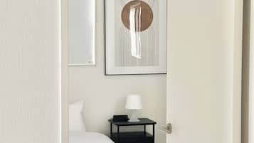 A hotel room with a bed, a bedside table with a lamp, a wall-mounted artwork, and a door.