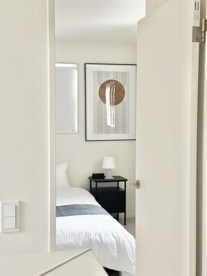 A hotel room with a bed, a bedside table with a lamp, a wall-mounted artwork, and a door. - JP Ozu Units By Restavio (Ozu)