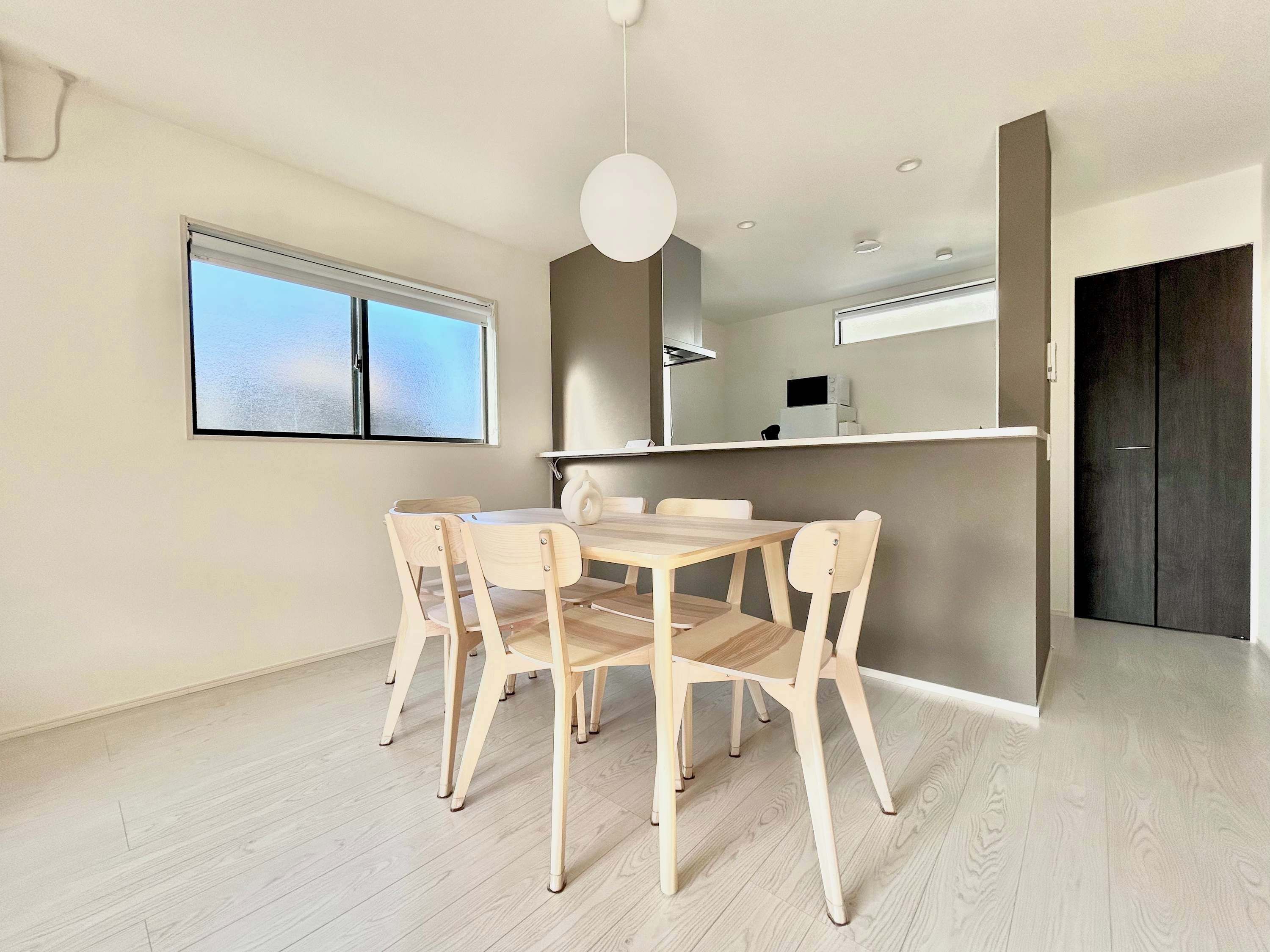 A modern dining area with a wooden table and chairs, a large window, and a dark door.