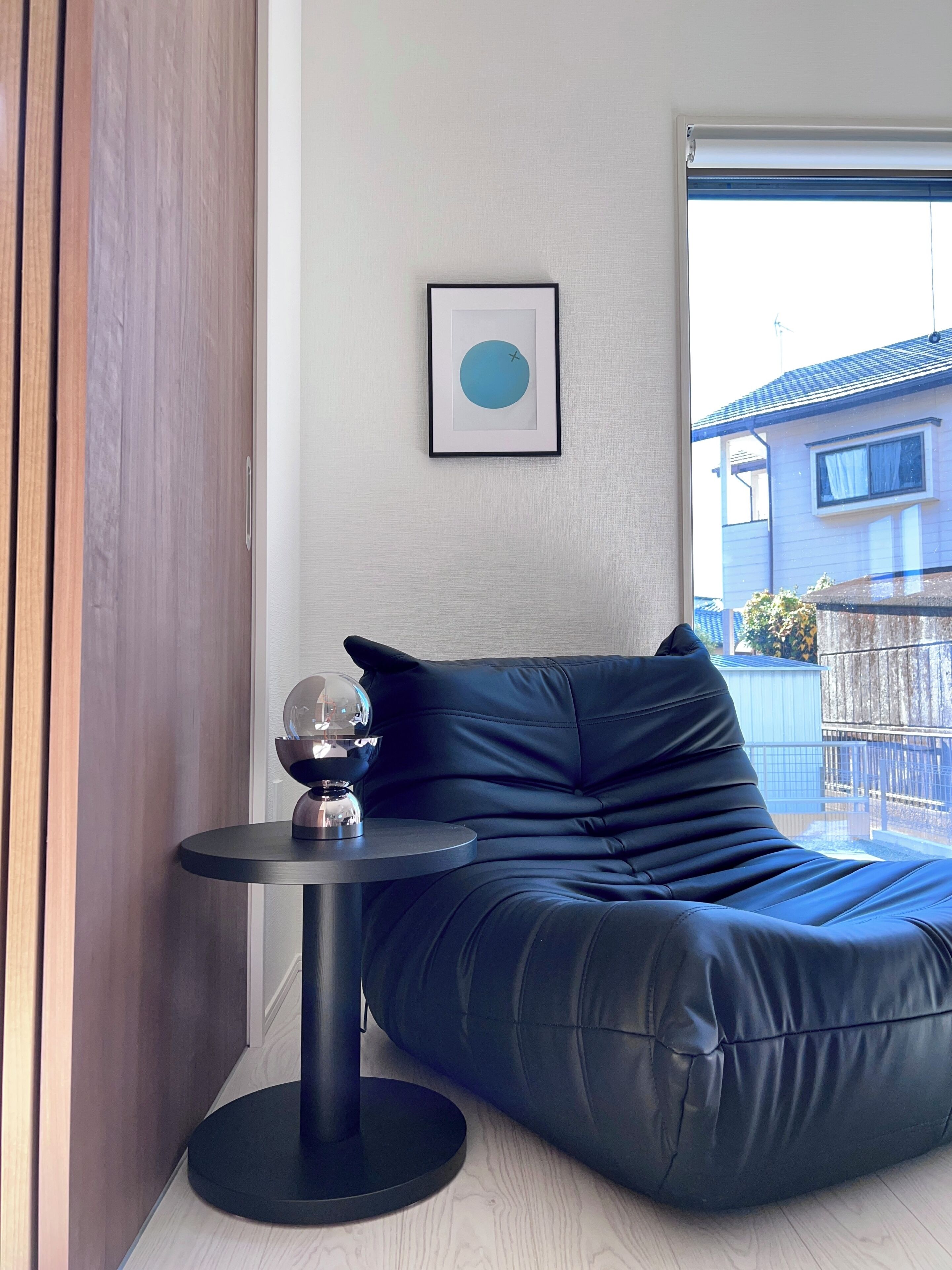 A modern room with a black leather sofa, a small round table with a decorative object, and a framed picture on the wall.