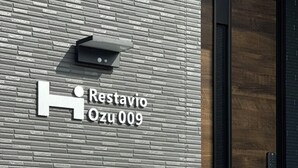 Moderni julkisivu, jossa on tiilikuviota, musta ovi ja kyltti, jossa lukee: ”Restavio Ozu 009”.