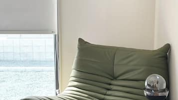 A green bean bag chair with a small table beside it, a framed picture on the wall, and a window with a view.