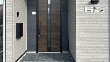 A modern building entrance with a dark wooden door, a small mailbox, and a sign indicating 'Restavio Ozu 005'.