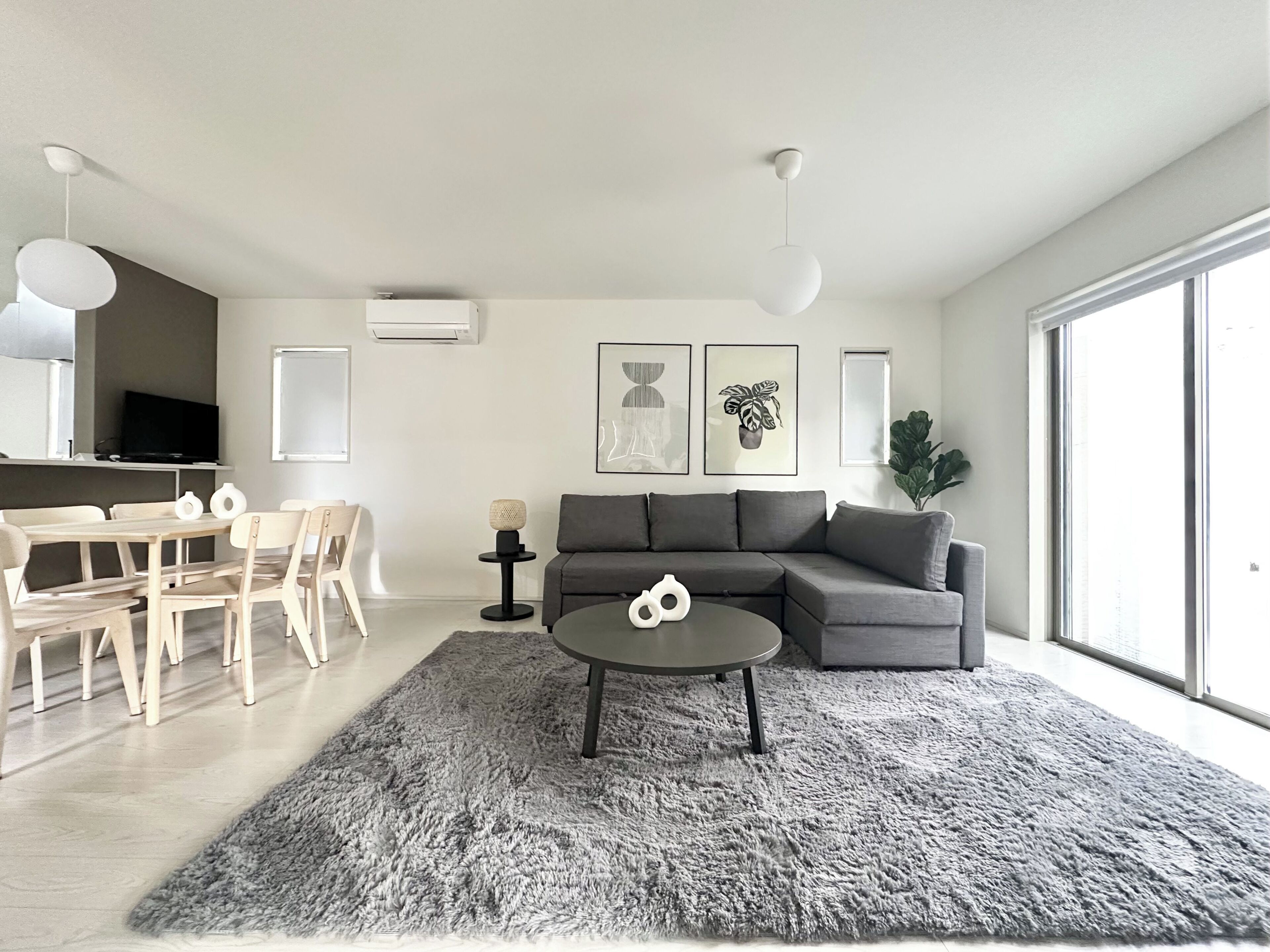 A modern living room with a grey sofa, a round coffee table, and a dining area with a table and chairs.