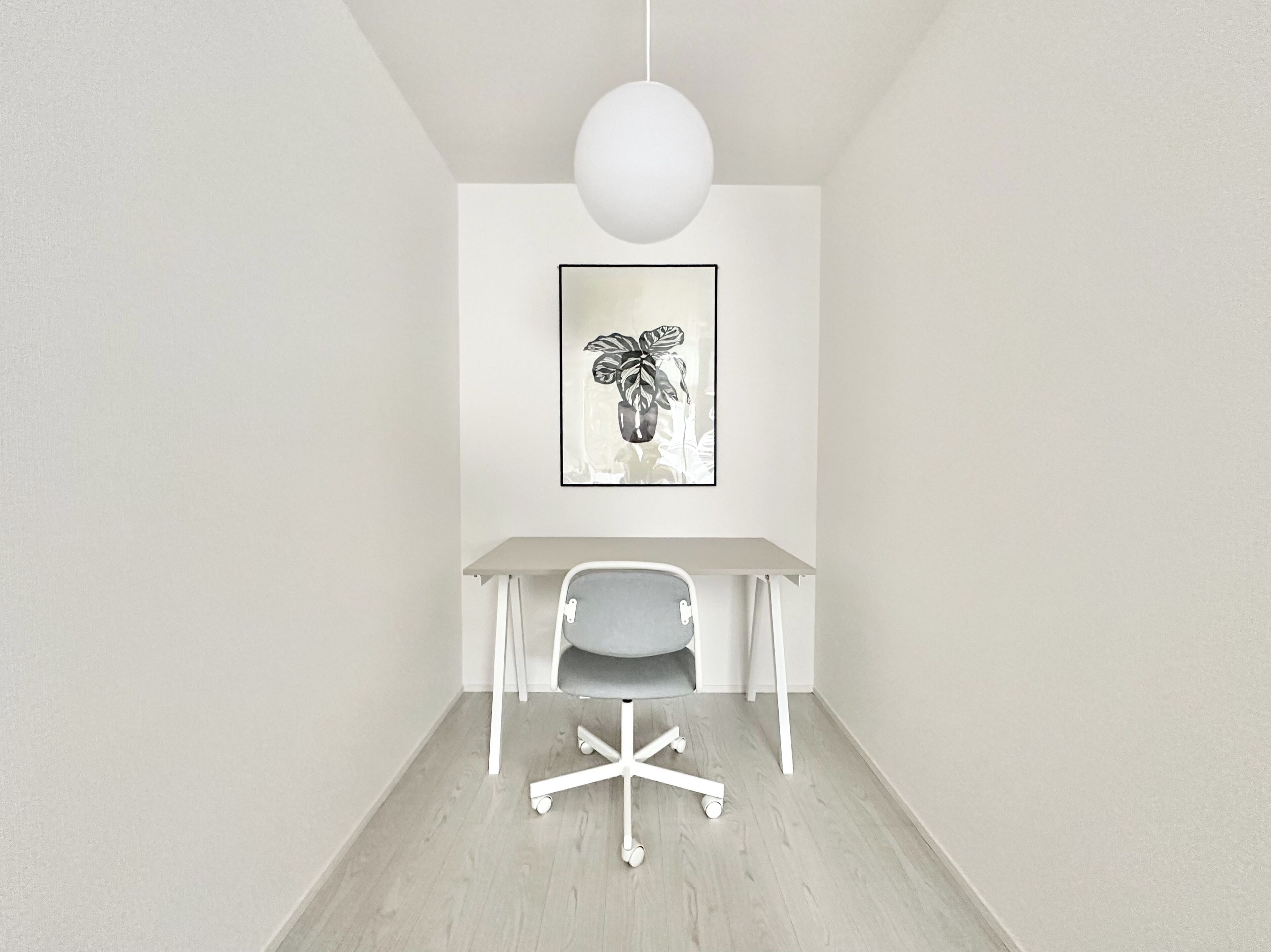 A minimalist office space with a white desk, a single office chair, and a framed artwork on the wall.
