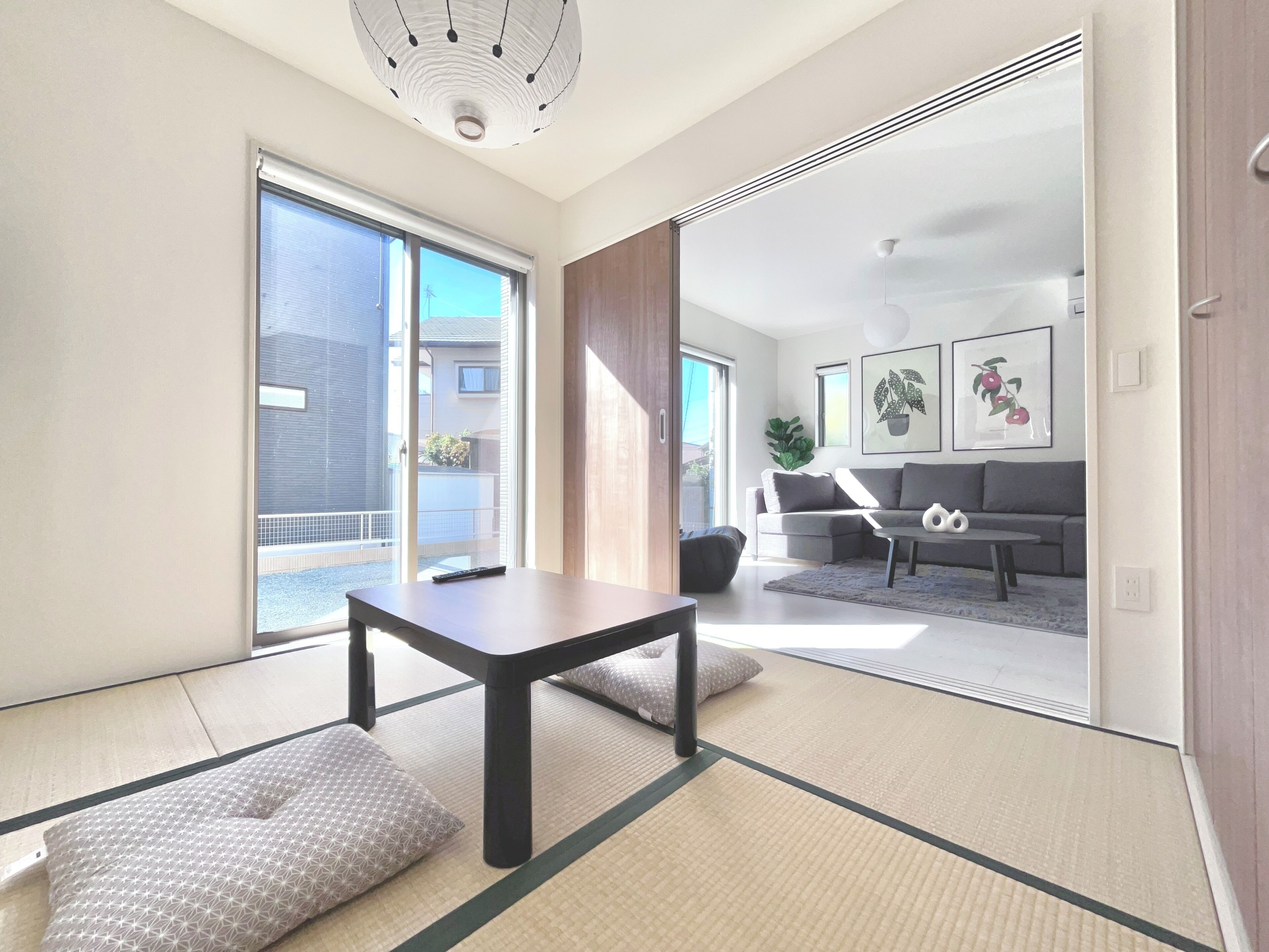 A modern living room with tatami flooring, a sofa, a coffee table, and a sliding glass door leading to a balcony.