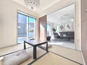A modern living room with tatami flooring, a sofa, a coffee table, and a sliding glass door leading to a balcony. - JP Ozu Units By Restavio (Ozu)