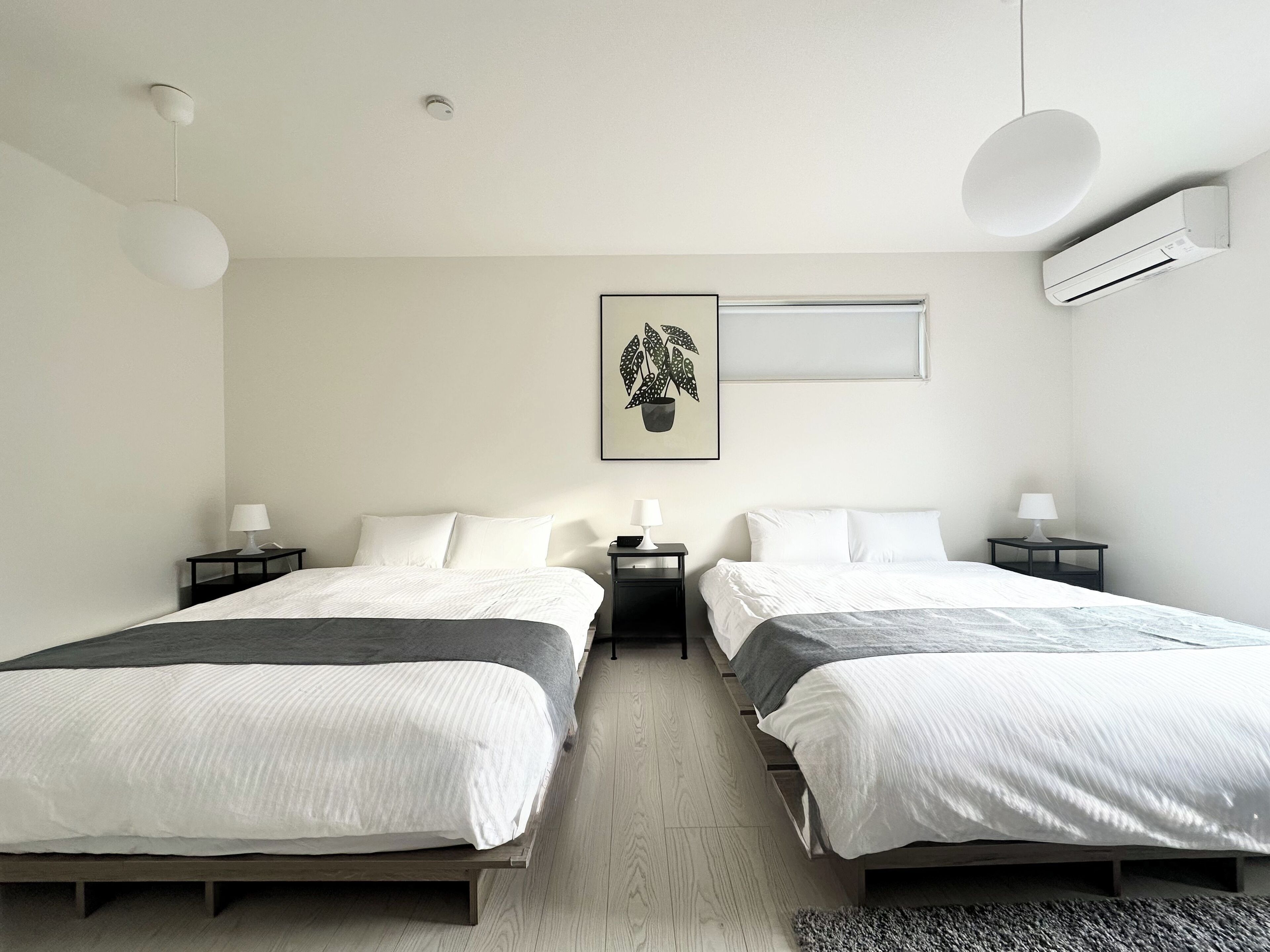 Habitación de hotel moderna con dos camas, aire acondicionado montado en la pared y una planta en marco.