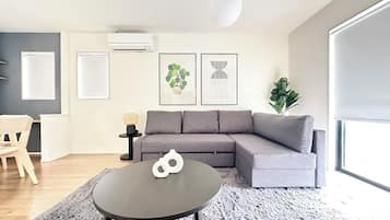 A modern living room with a grey sofa, a round coffee table, and a large window.