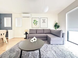 Un moderno salón con un sofá gris, una mesa redonda de centro y un ventanal grande.