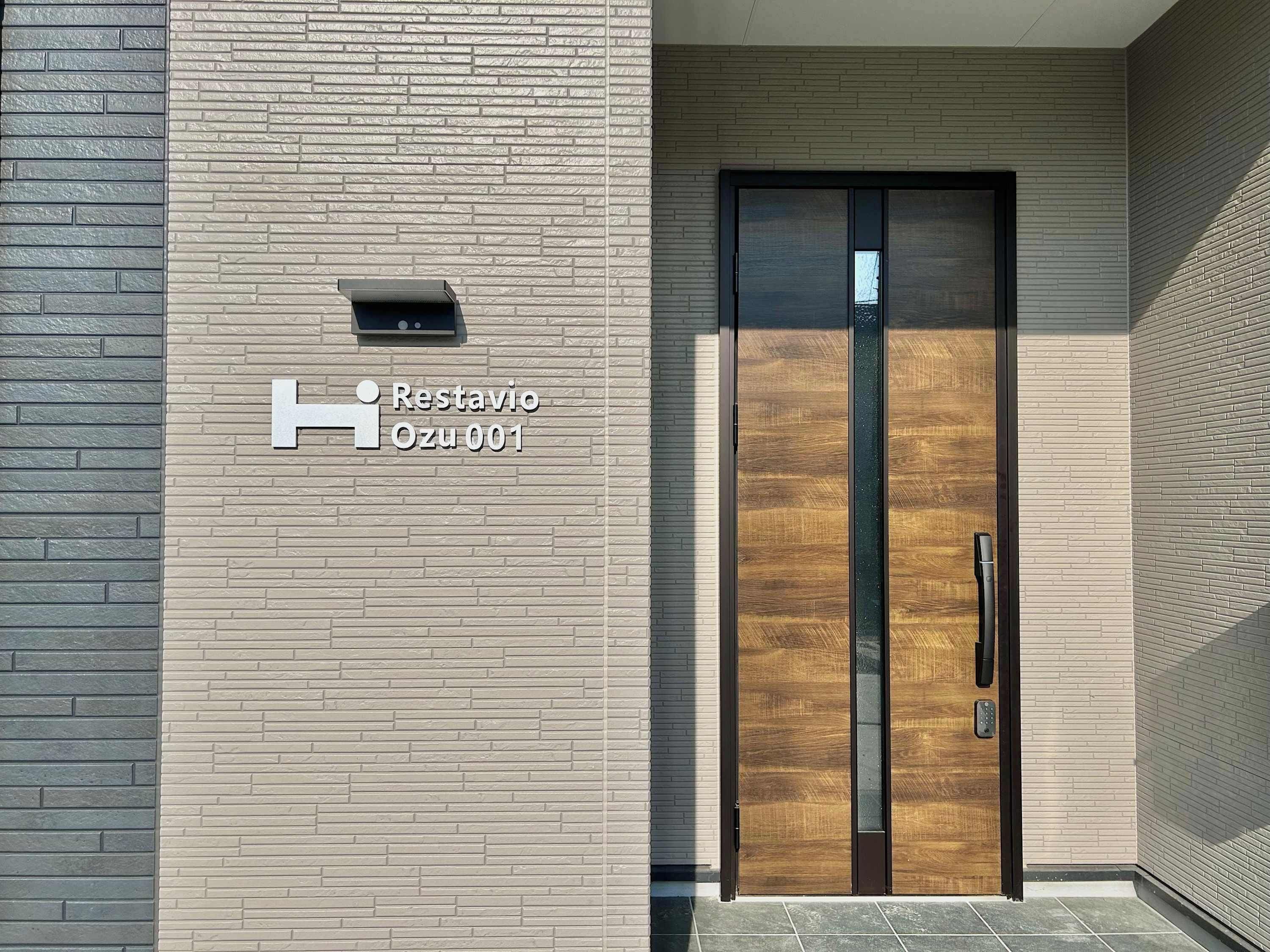 A modern building facade with a sign reading "Restavio Ozu 001" and a double door with a handle.