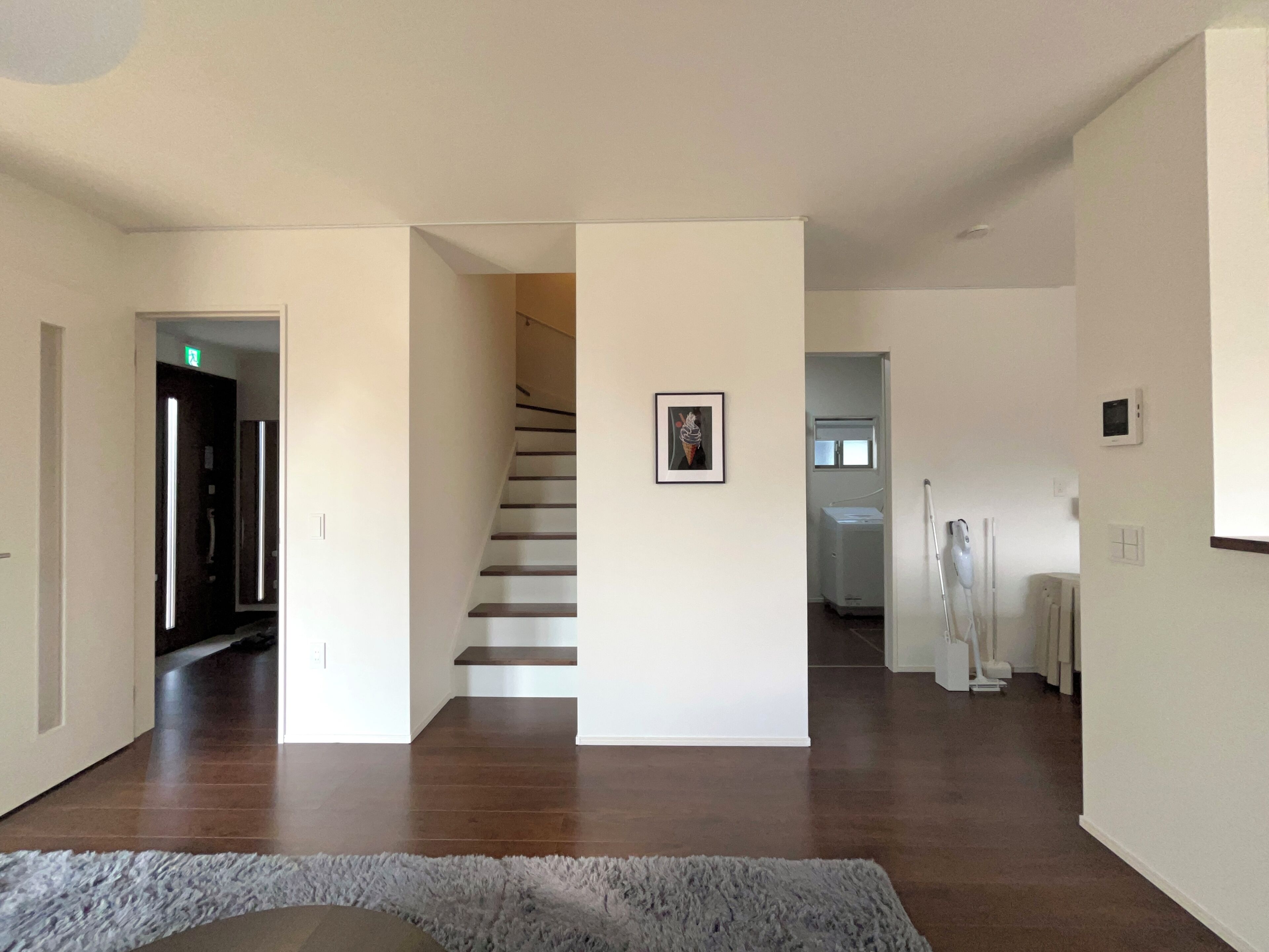 A spacious hallway with a wooden floor, a staircase, and a framed picture on the wall.