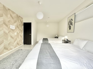 A modern hotel room with two beds, a large window, a wooden herringbone wall, and a single artwork.