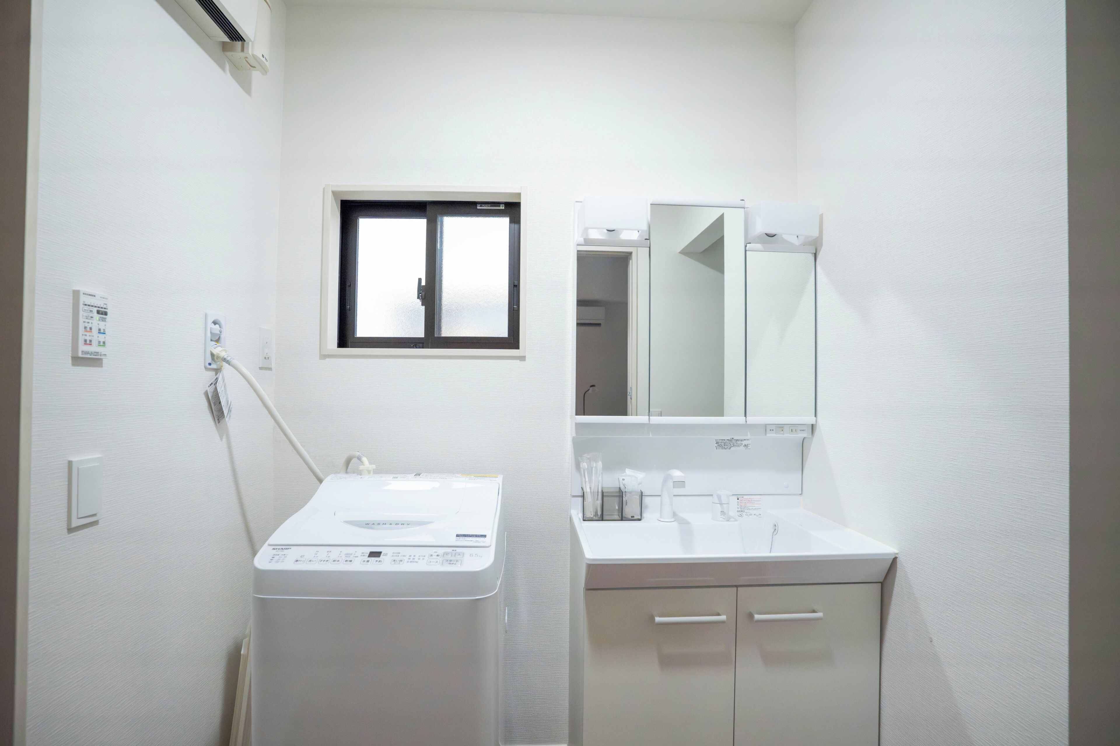 A compact bathroom with a washing machine, a sink, and a mirror.