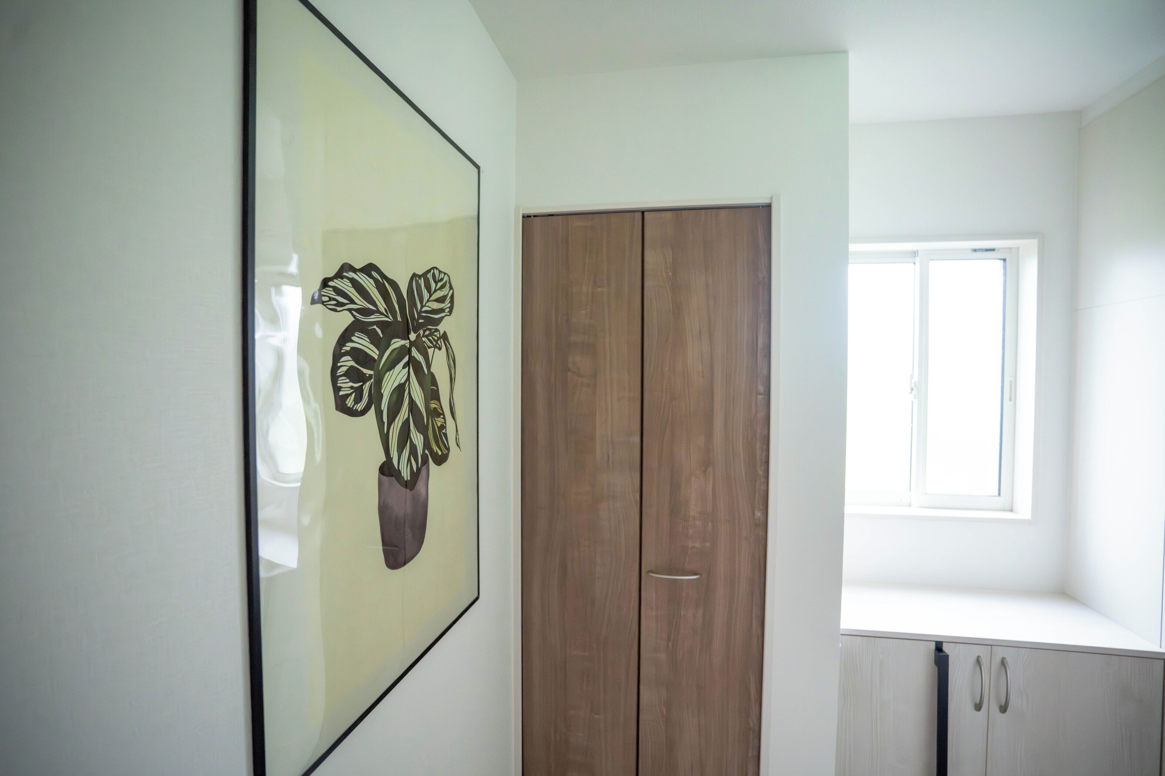 A room with a wooden wardrobe, a window, and a framed artwork on the wall.