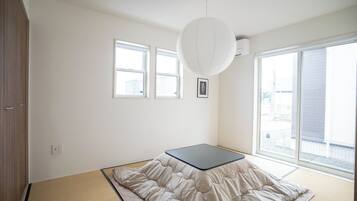 Ett rum med tatamimattor på golvet, en futonmadrass, ett stort fönster och en taklampa.