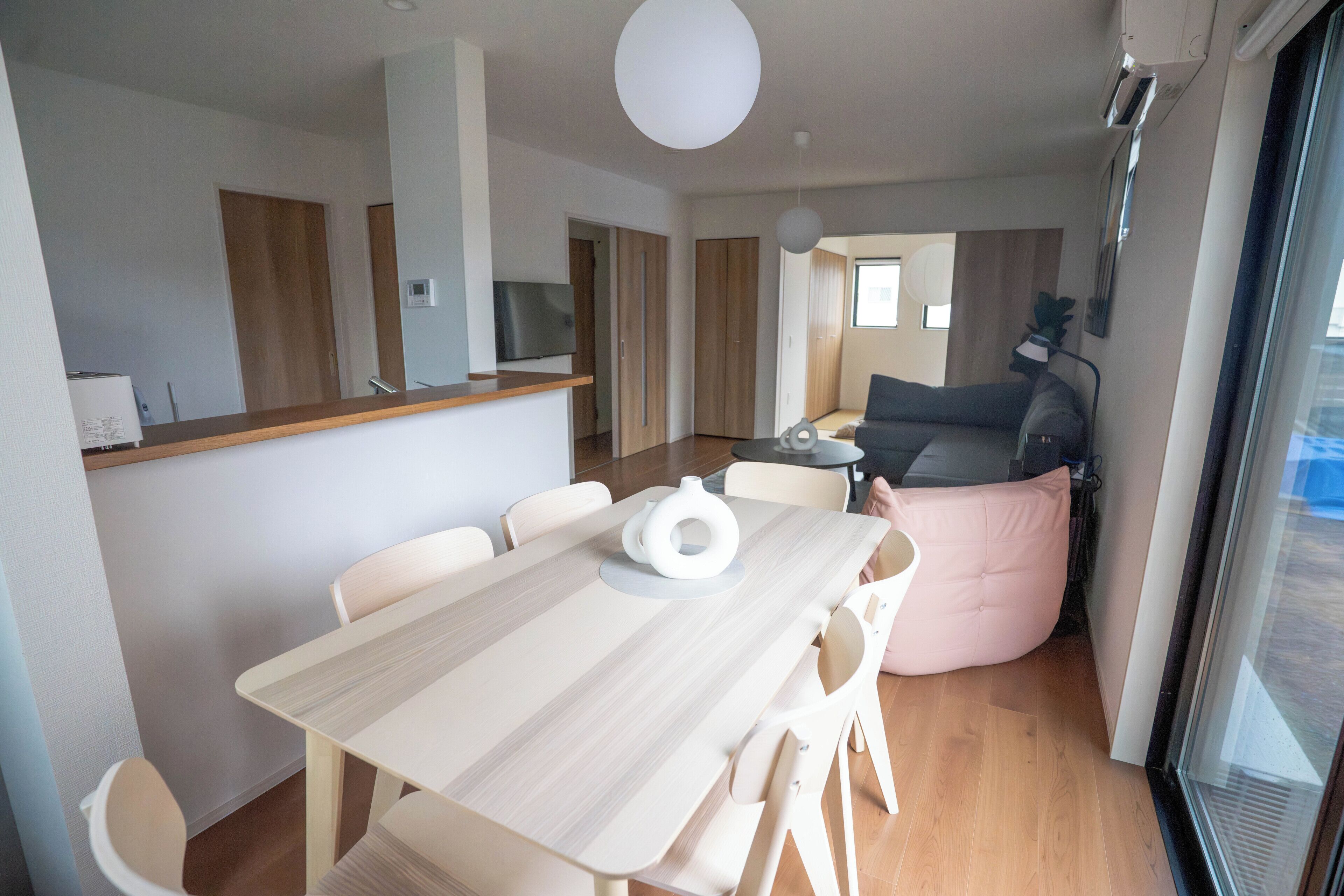 A modern kitchen with a dining area, a sofa, and a large window.