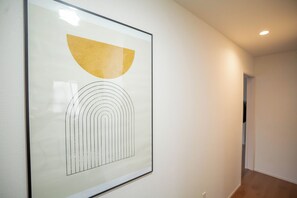 A framed artwork with abstract geometric shapes on a plain wall in a hallway.