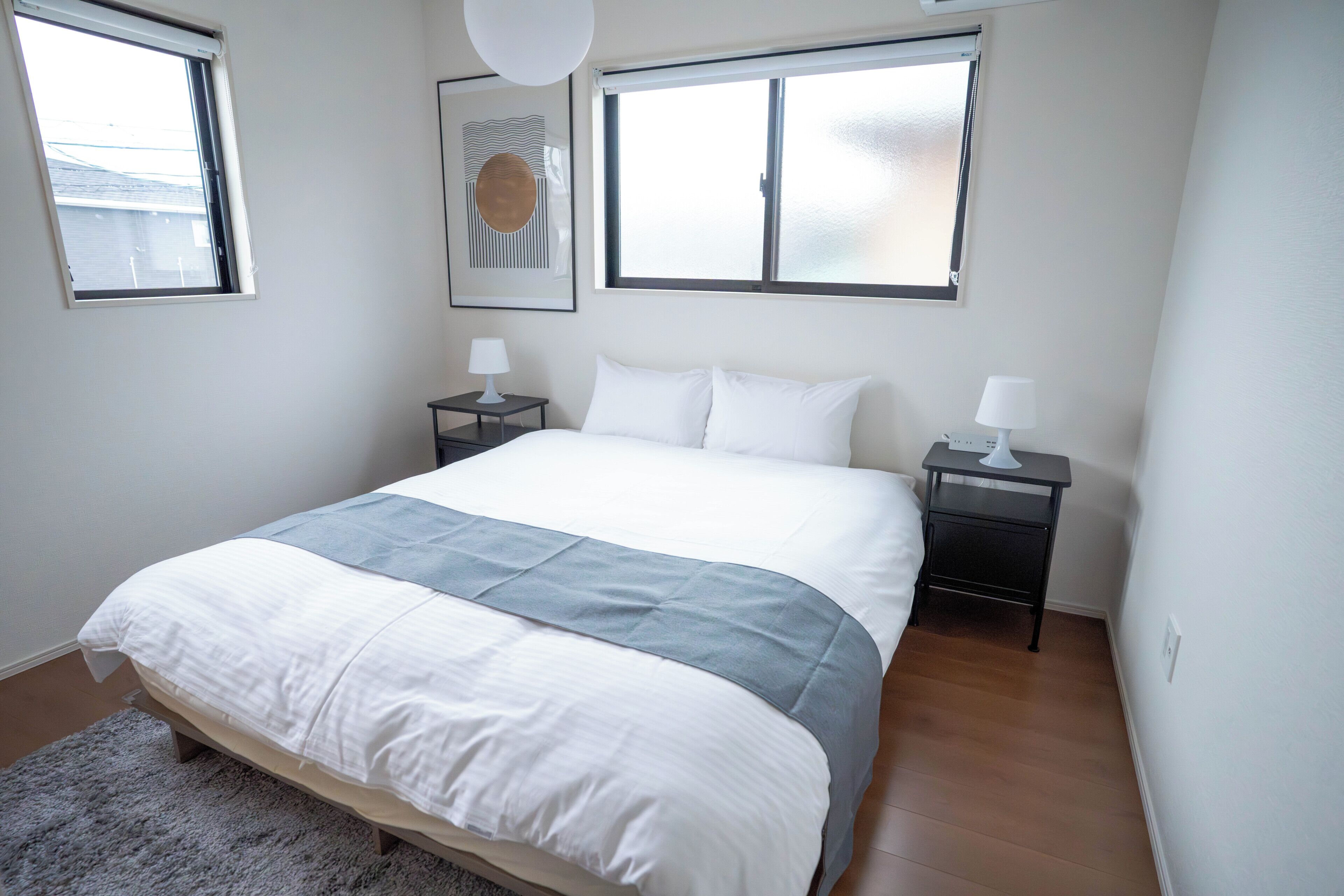 Une chambre à coucher avec un lit, deux tables de chevet, un tapis et deux fenêtres.