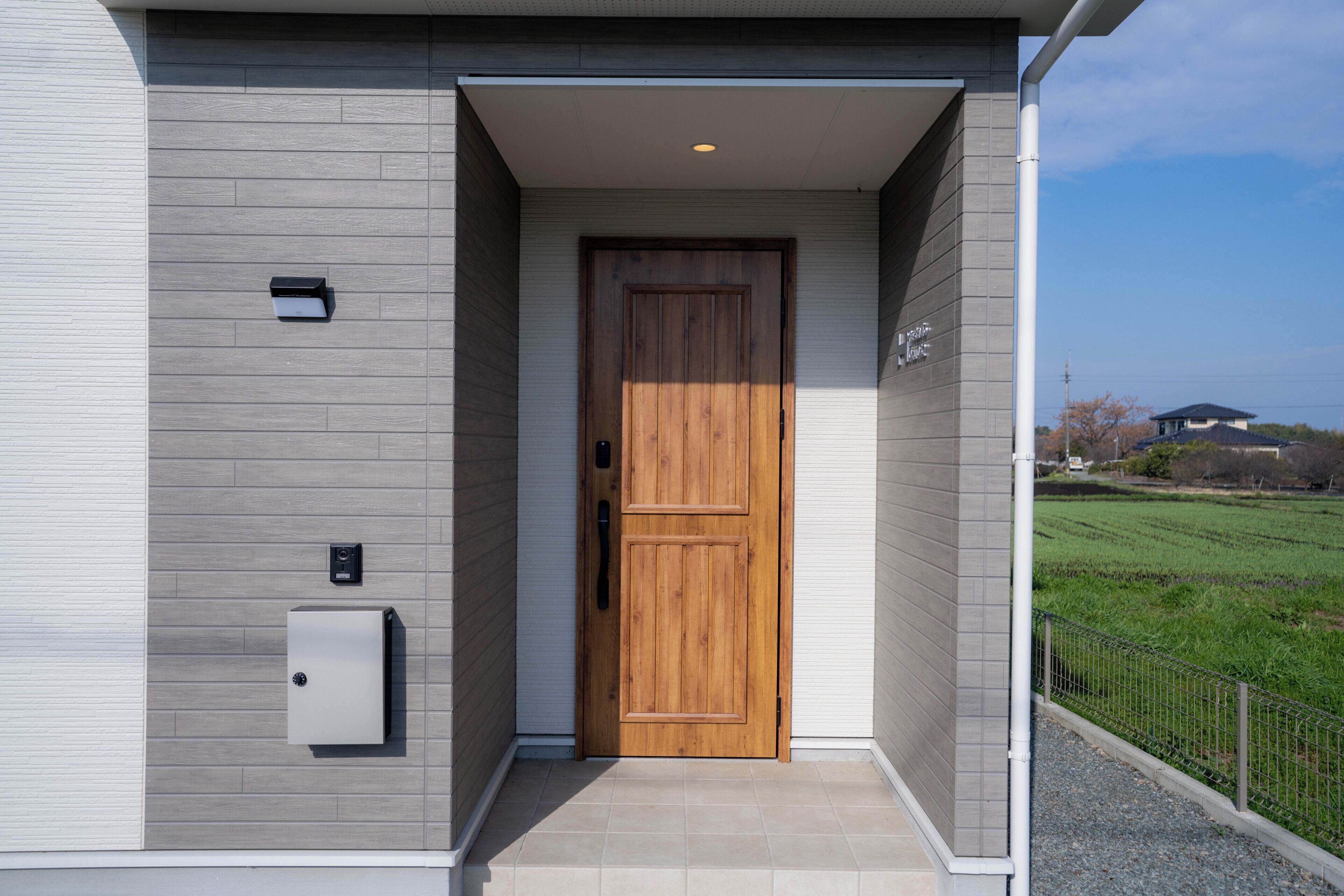 A modern building entrance with a wooden door, a security camera, and a mailbox.