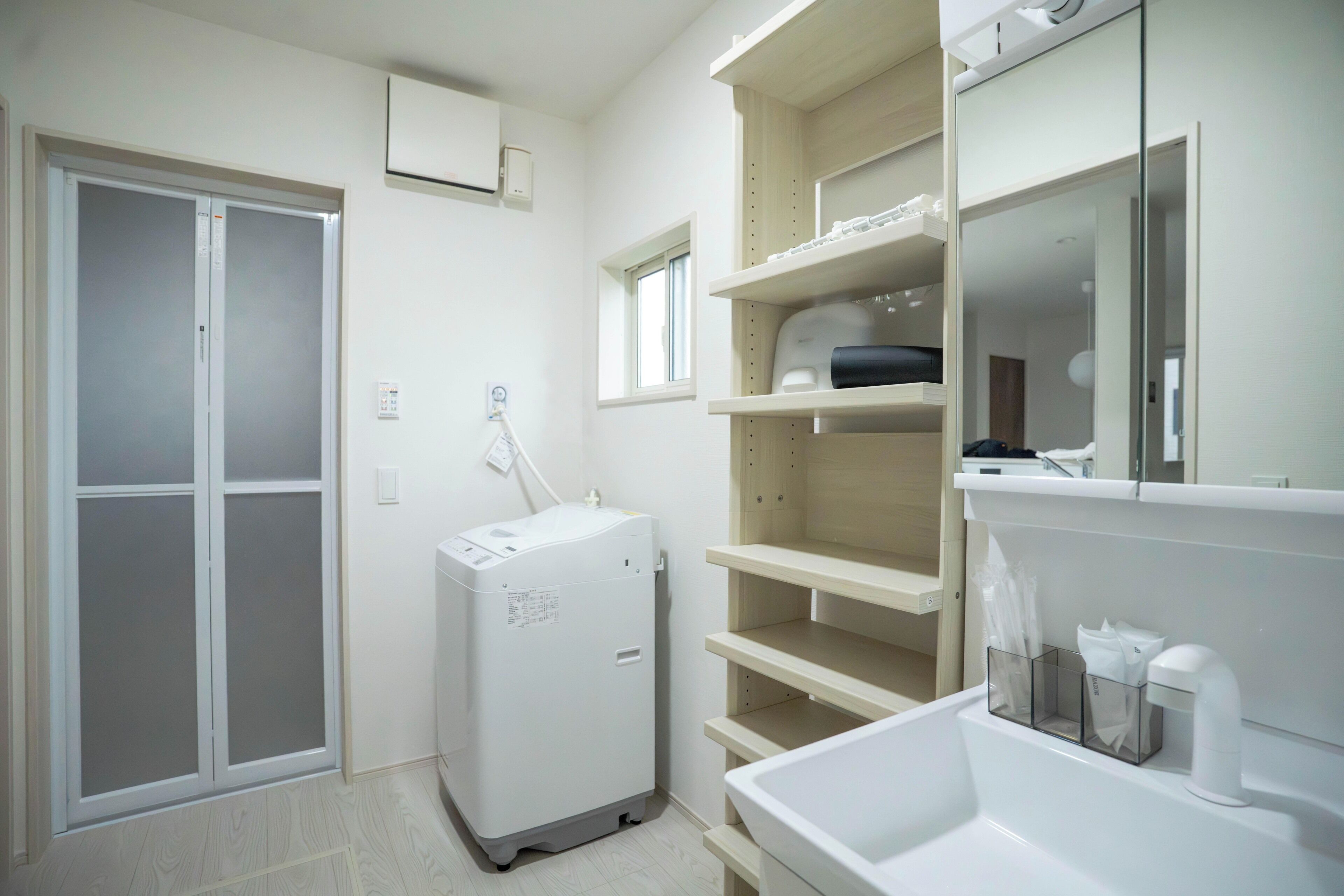 A hotel room with a wardrobe, a small appliance, and a bathroom with a mirror and shelves.