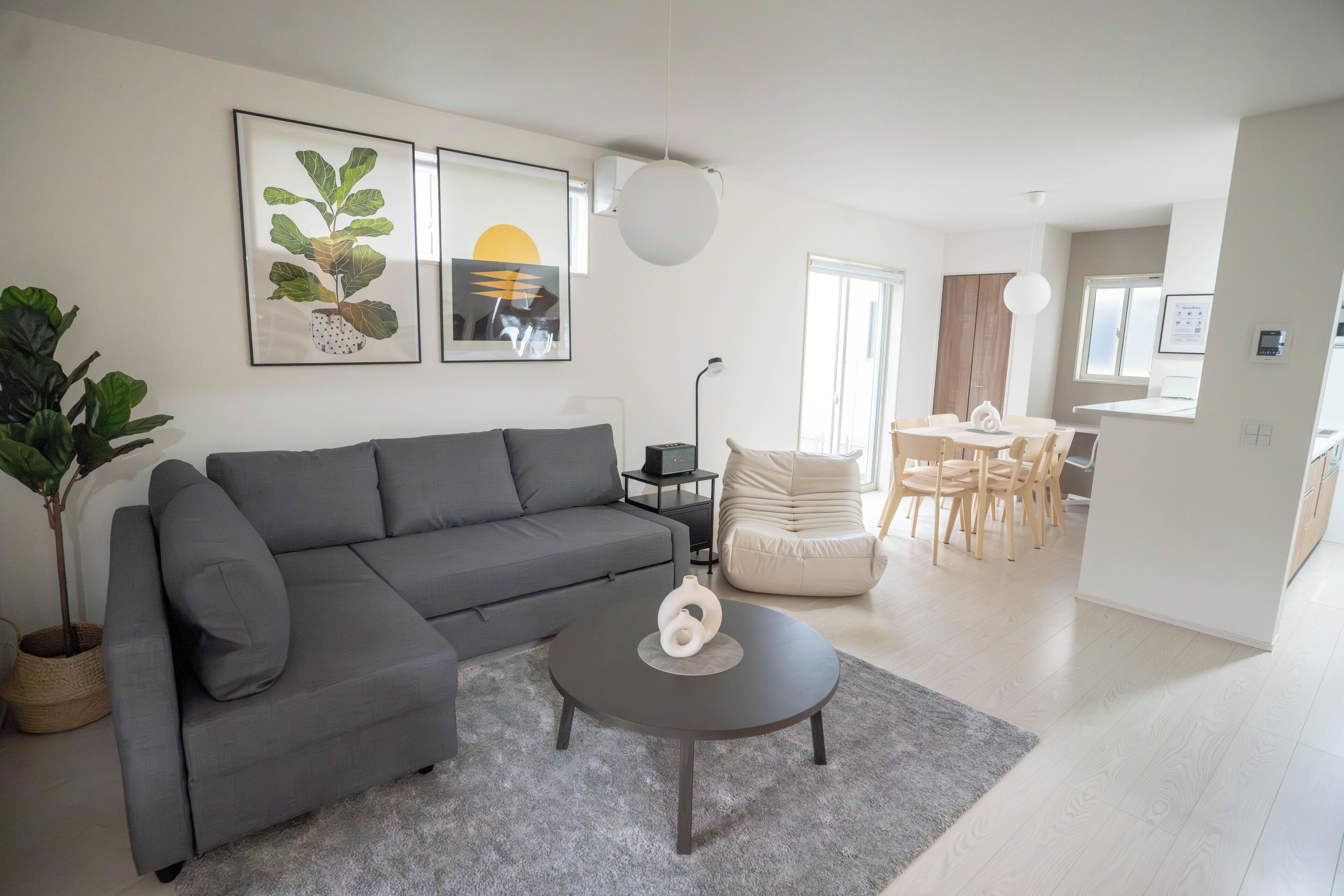 Een moderne woonkamer met een grijze bank, een salontafel en een eethoek met een tafel en stoelen.