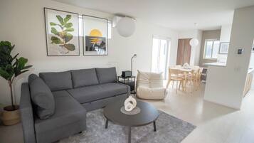 Een moderne woonkamer met een grijze bank, een salontafel en een eethoek met een tafel en stoelen.