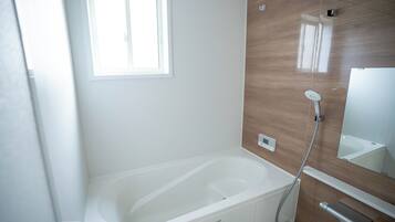 A modern bathroom with a freestanding bathtub, a handheld showerhead, and a wall-mounted control panel.