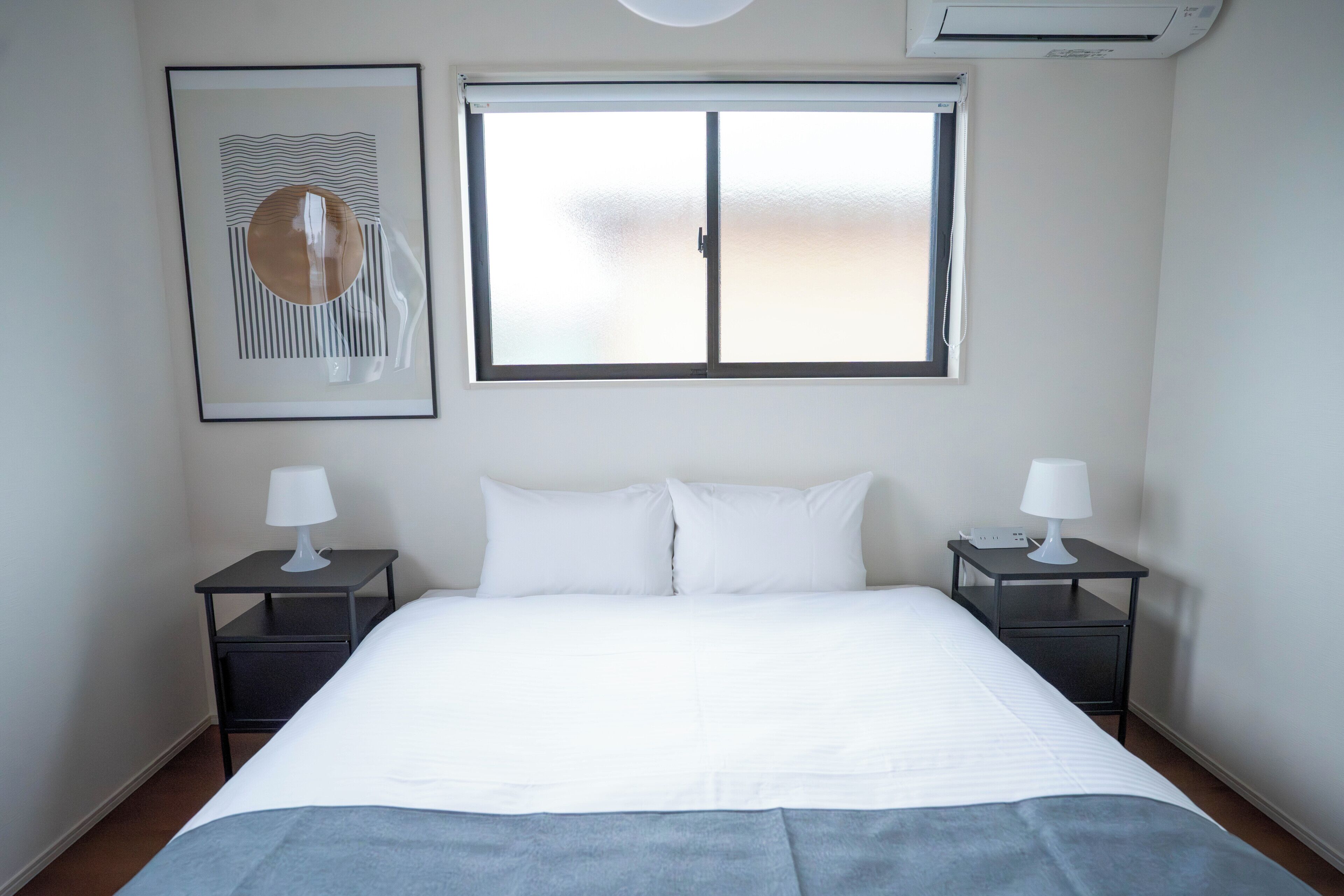 Een hotelkamer met een bed, twee nachtkastjes, een raam en een wandairconditioner.