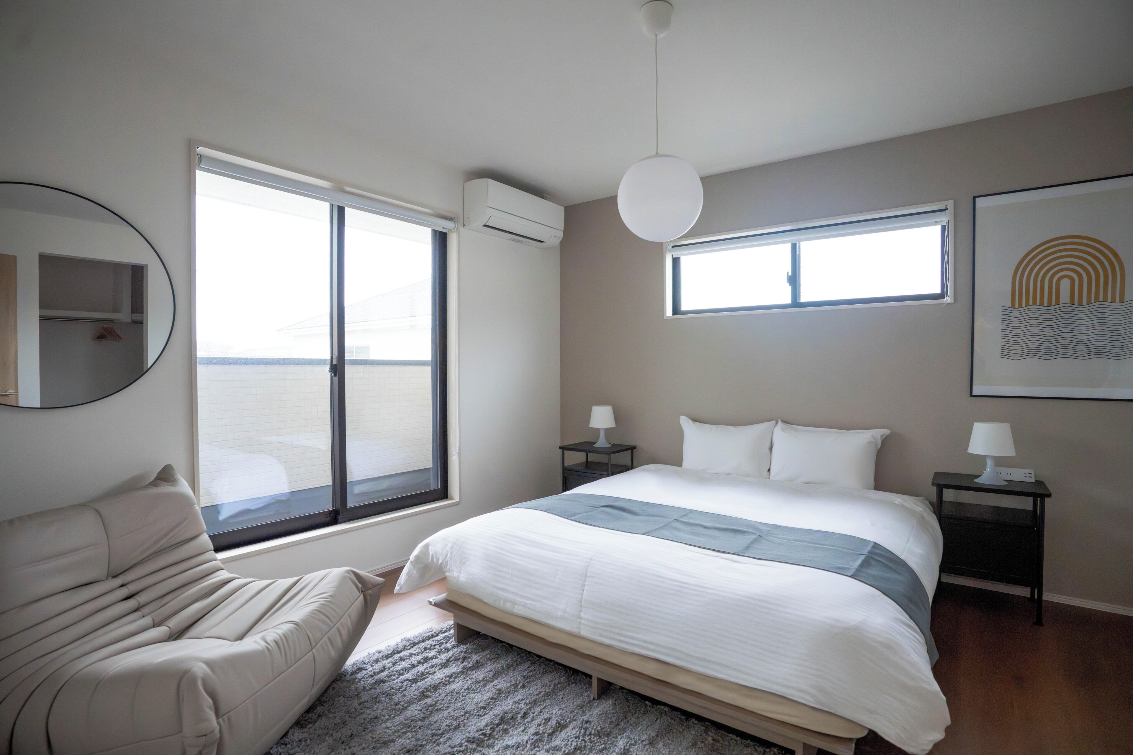 A modern bedroom with a bed, a chair, a desk, and a large window.