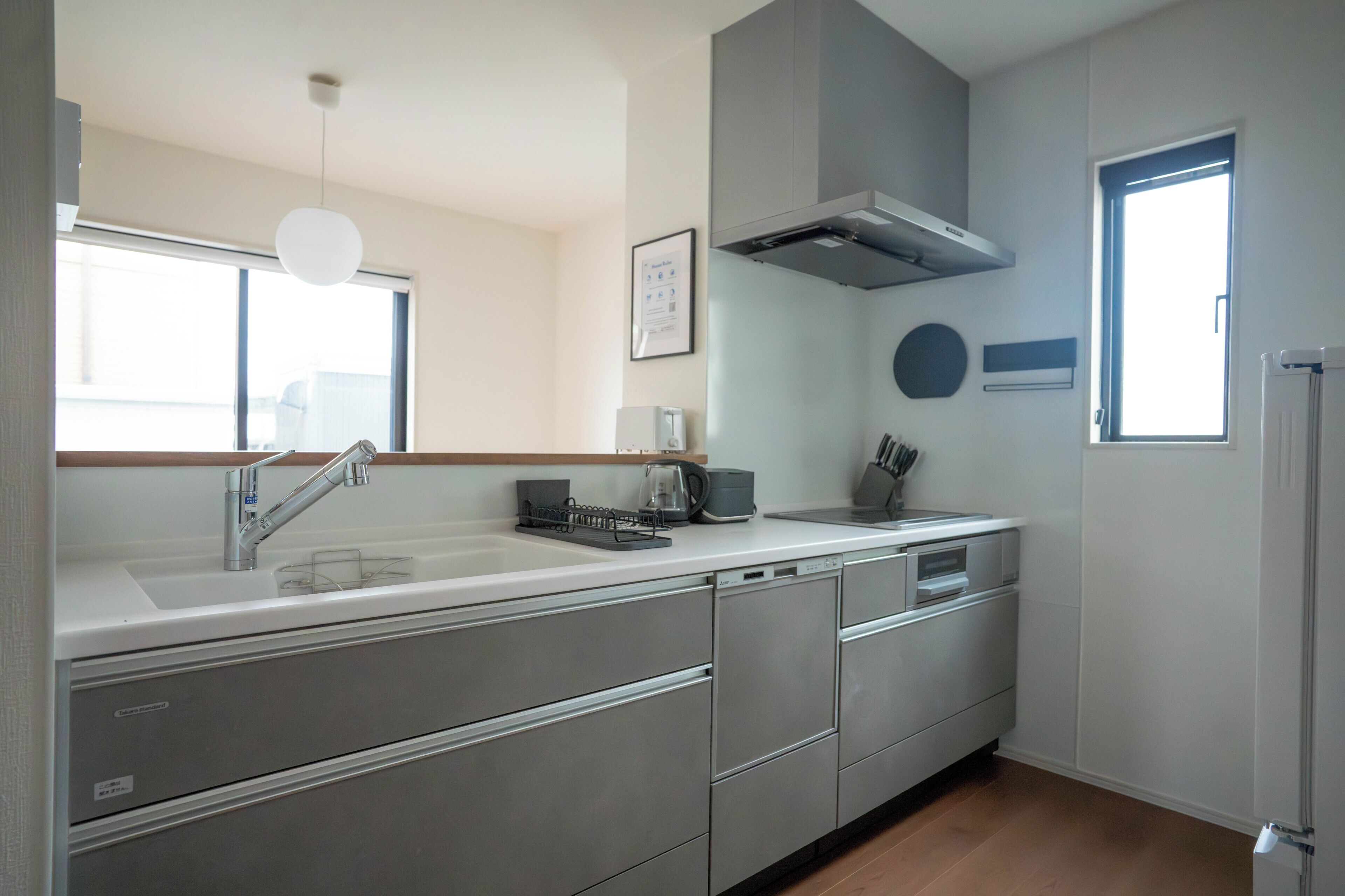 A modern kitchen with a built-in dishwasher, stainless steel cabinets, a range hood, and a window providing natural light.