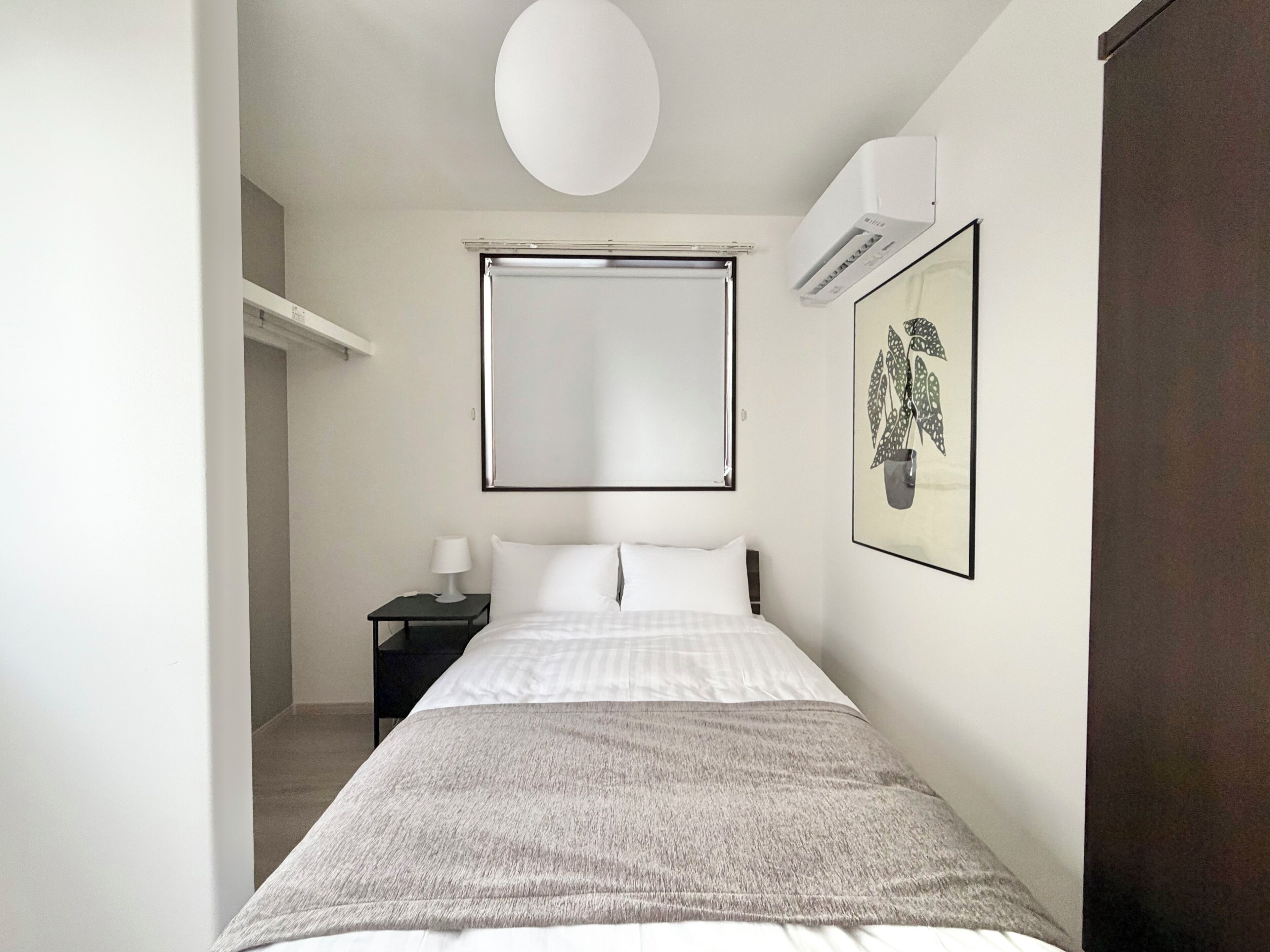 Um quarto com uma cama, mesa de cabeceira, luminária, ar-condicionado fixado na parede e um quadro emoldurado.
