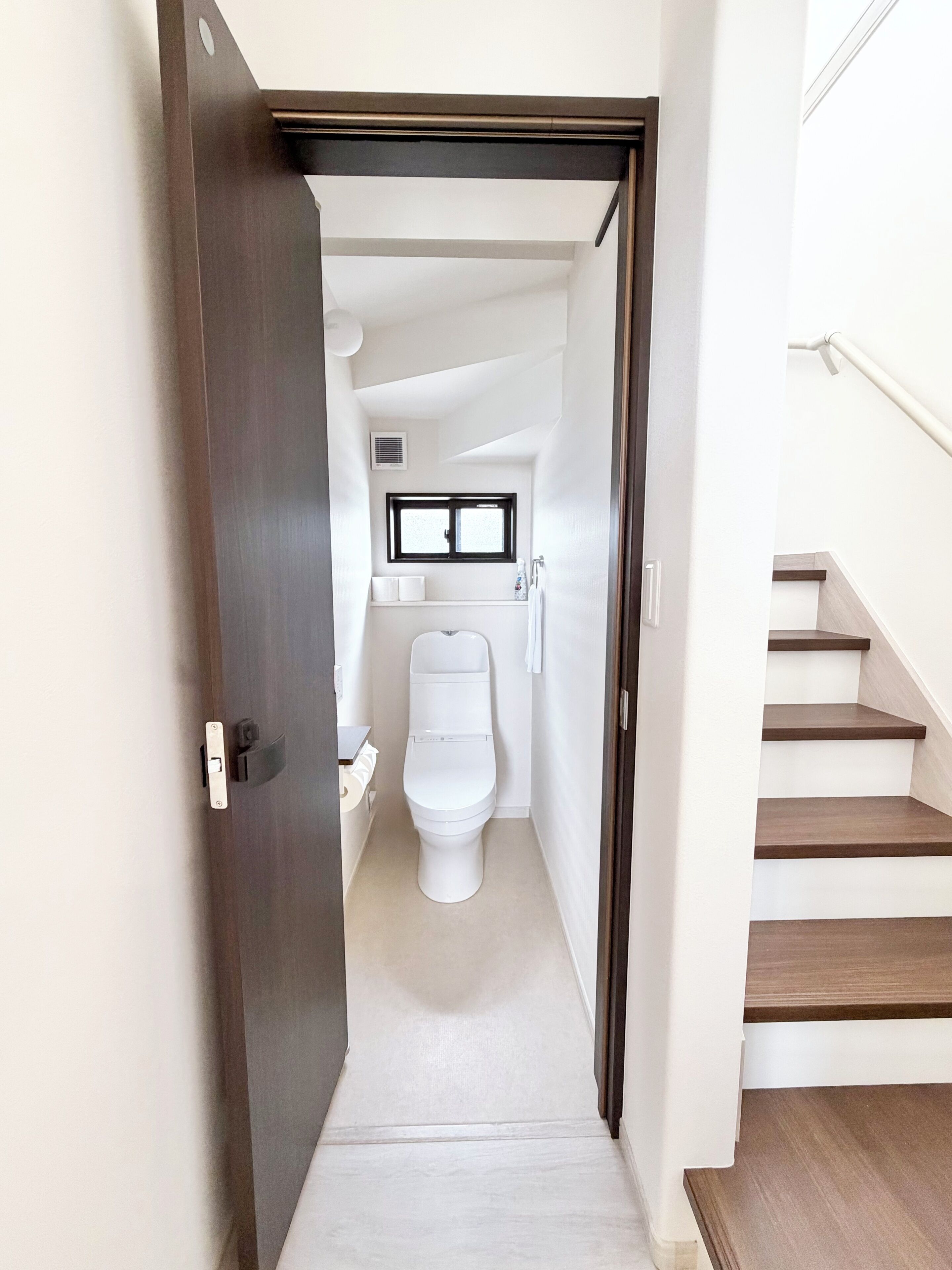 Un pasillo estrecho que conduce a un baño con inodoro, lavabo y ventana.