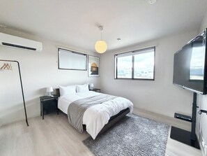 Ein modernes Schlafzimmer mit einem Bett, Nachttischen, einem Fernseher und einem großen Fenster.