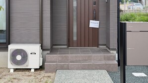 Ein modernes Gebäude mit einer braunen Tür, einem Schild mit der Aufschrift 'Restavio Ozu 053' und einer großen Klimaanlage links.