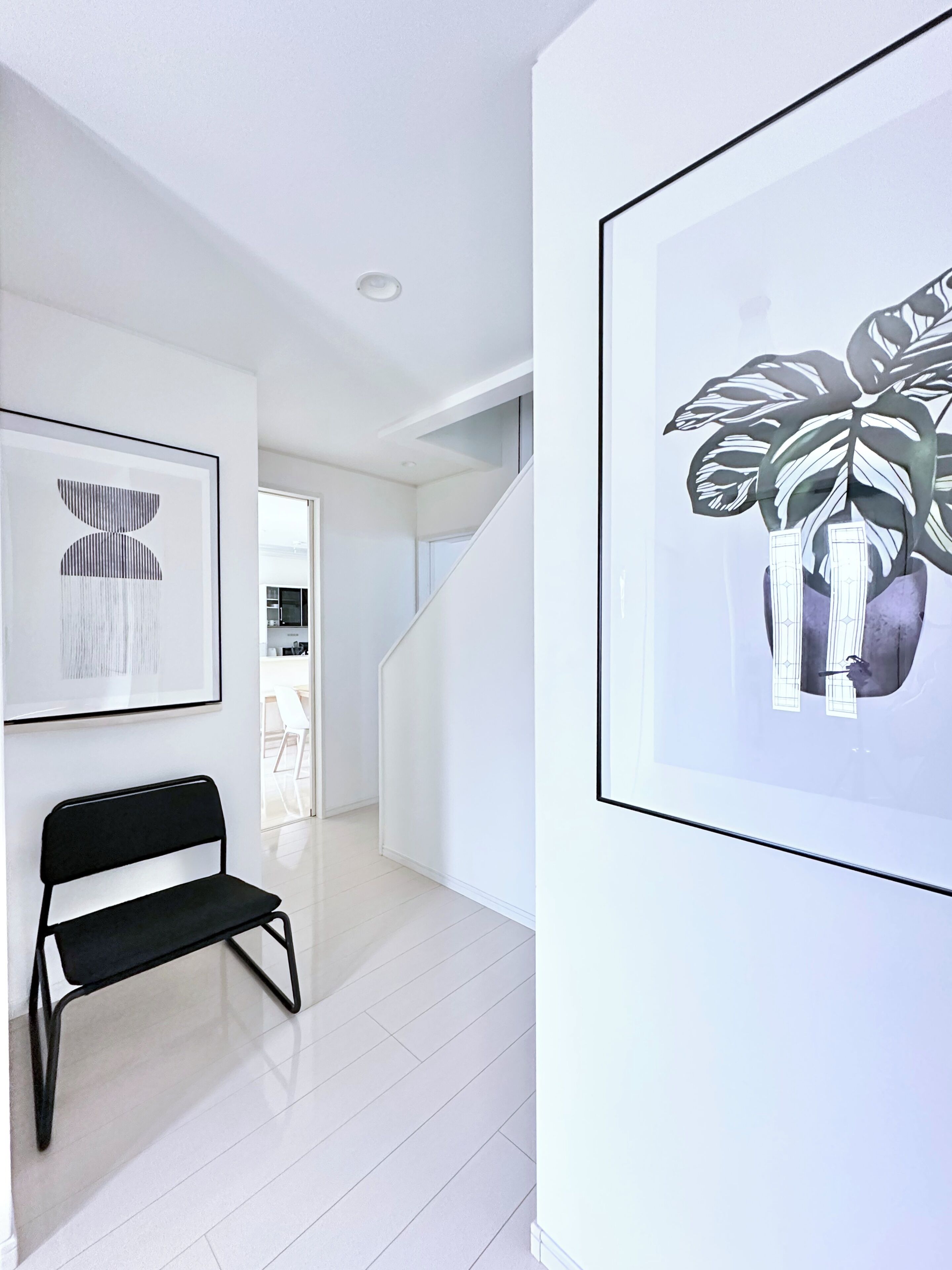 A hallway with a black bench, a framed abstract artwork, and a framed plant illustration on the wall.